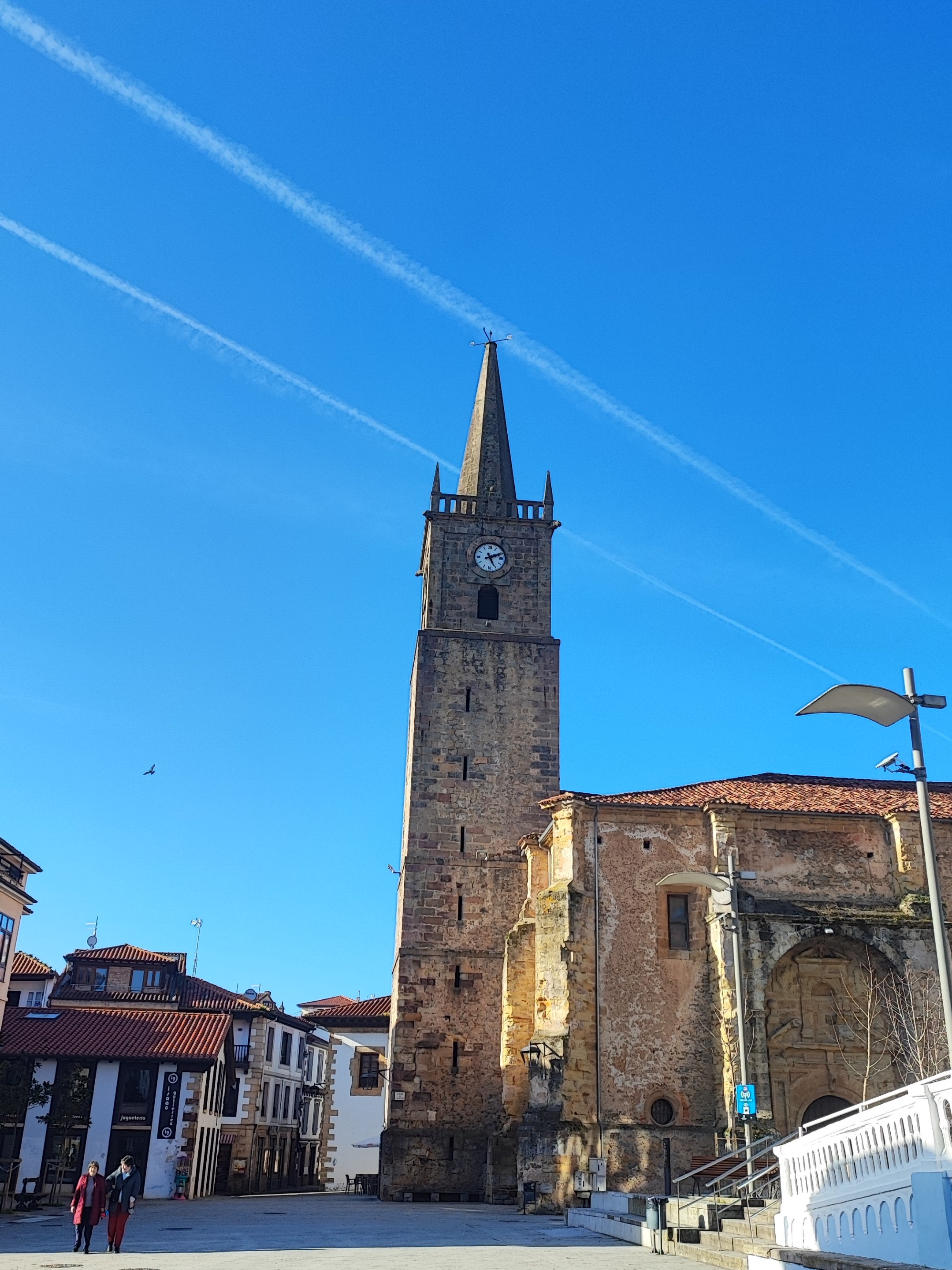 Tall stone clock tower against a blue sky in a town square.