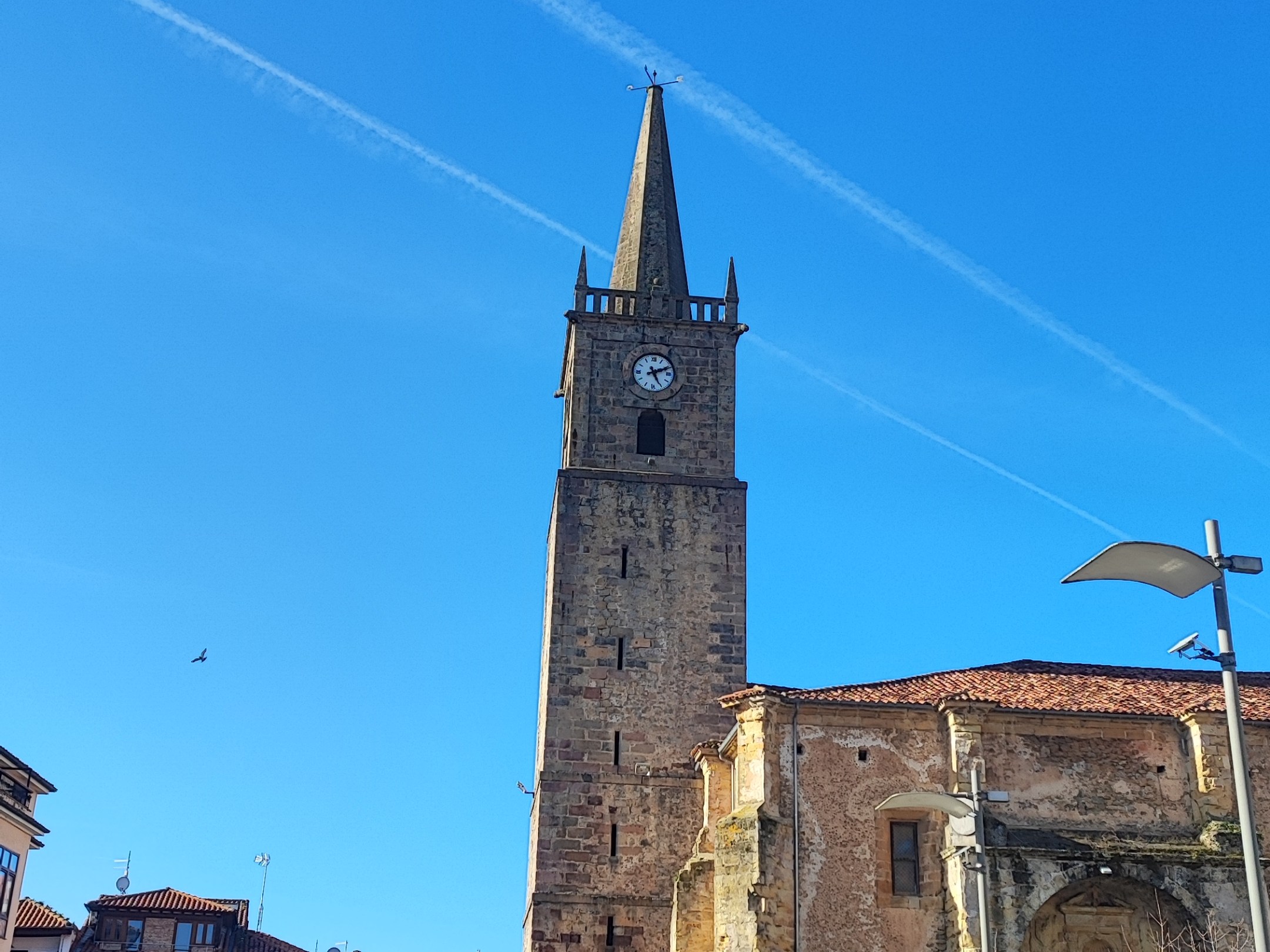 Tall stone clock tower against a blue sky in a town square.