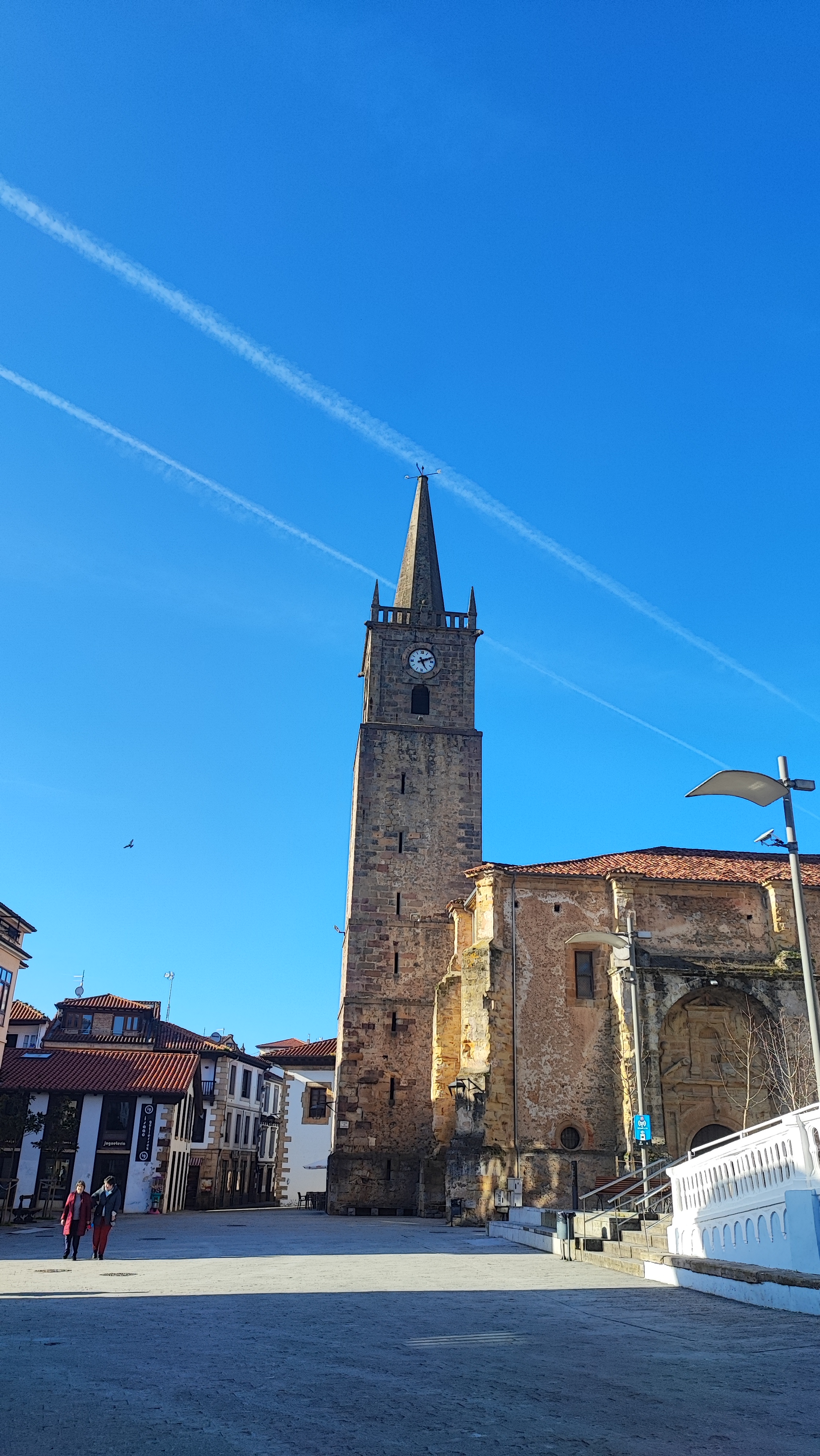Tall stone clock tower against a blue sky in a town square.