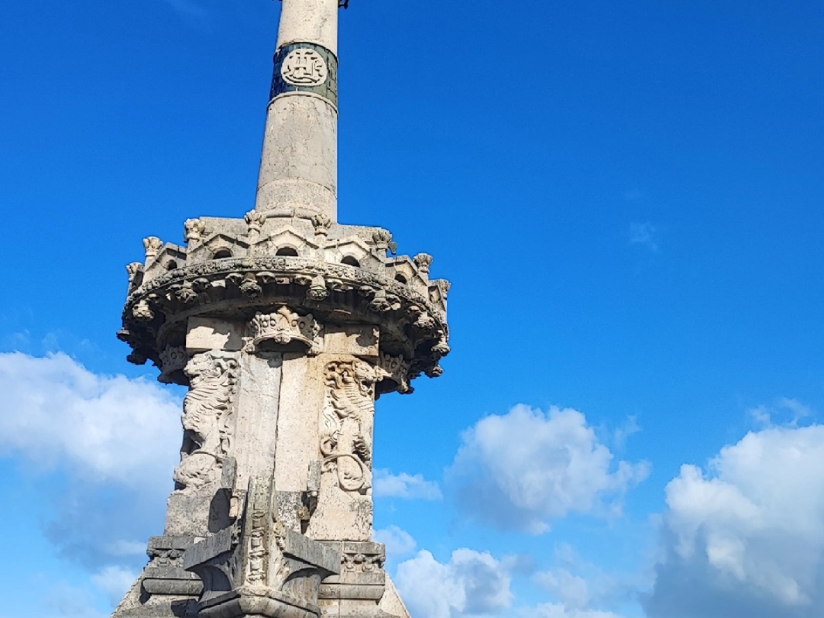 Stone monument with a statue on top near the ocean under a blue sky.