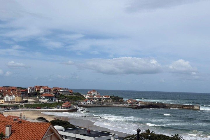 Coastal view with beach, houses, and ocean waves under a cloudy sky.
