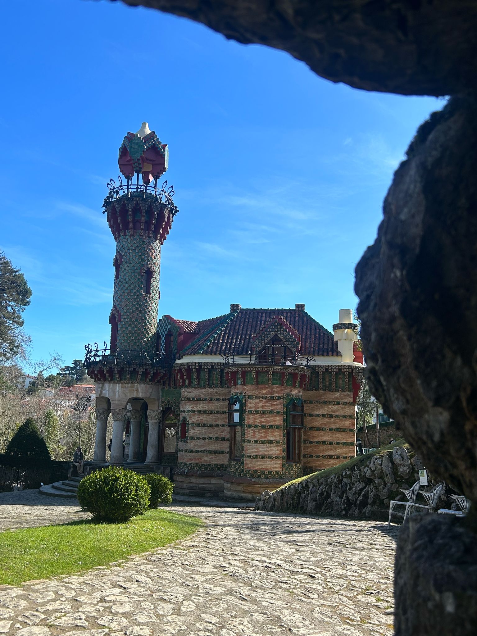 Colorful Gaudí-style building with tower and mosaic design on a sunny day.