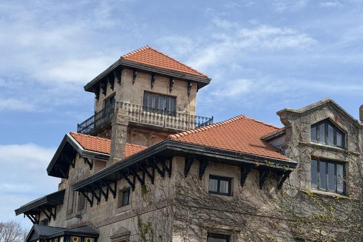Stone building with red-tiled roof and tall gabled tower against a blue sky.