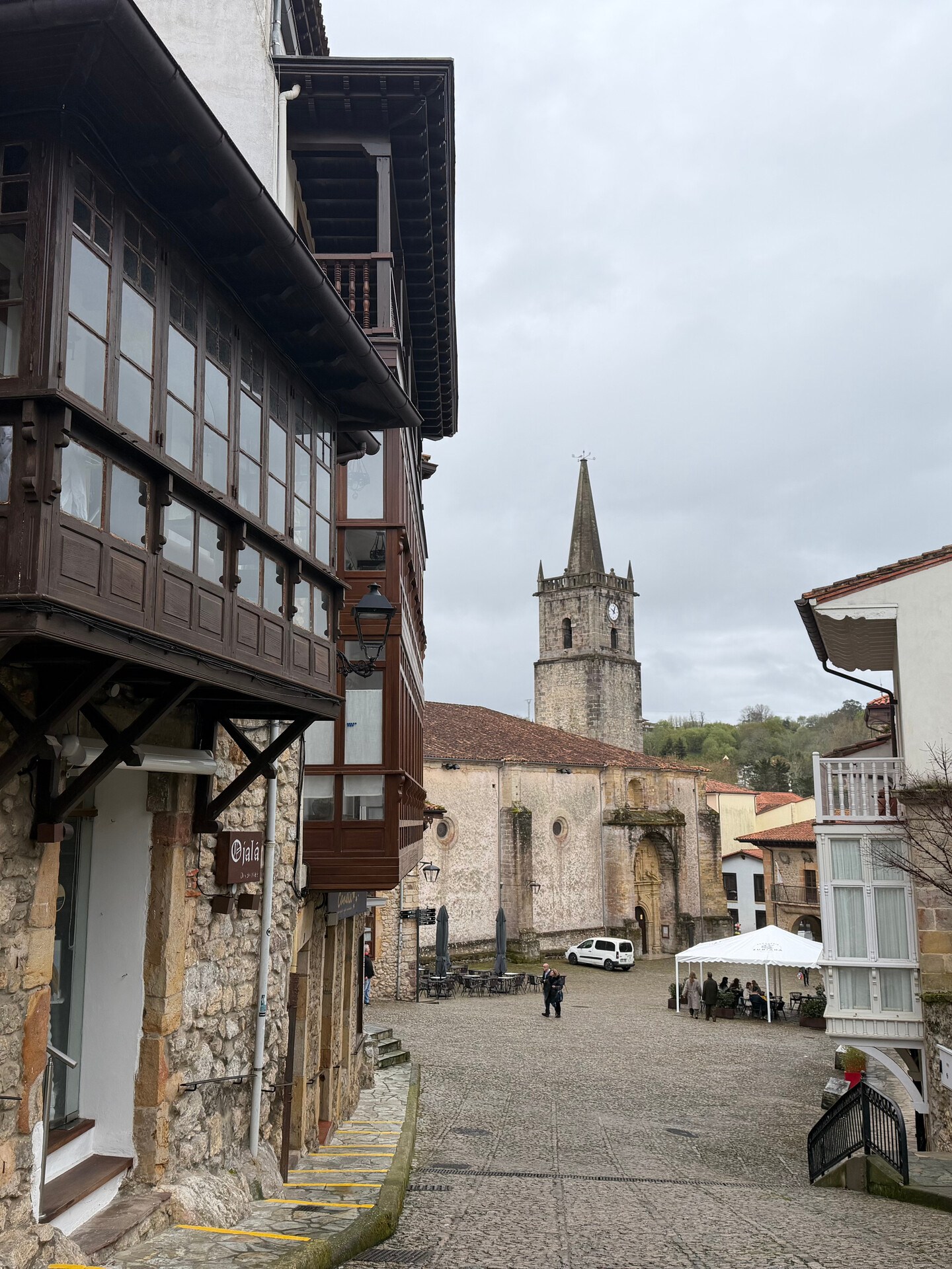Historic street with stone buildings and distant church tower on a cloudy day.