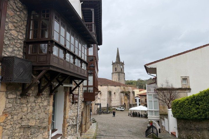 Historic street with stone buildings and distant church tower on a cloudy day.