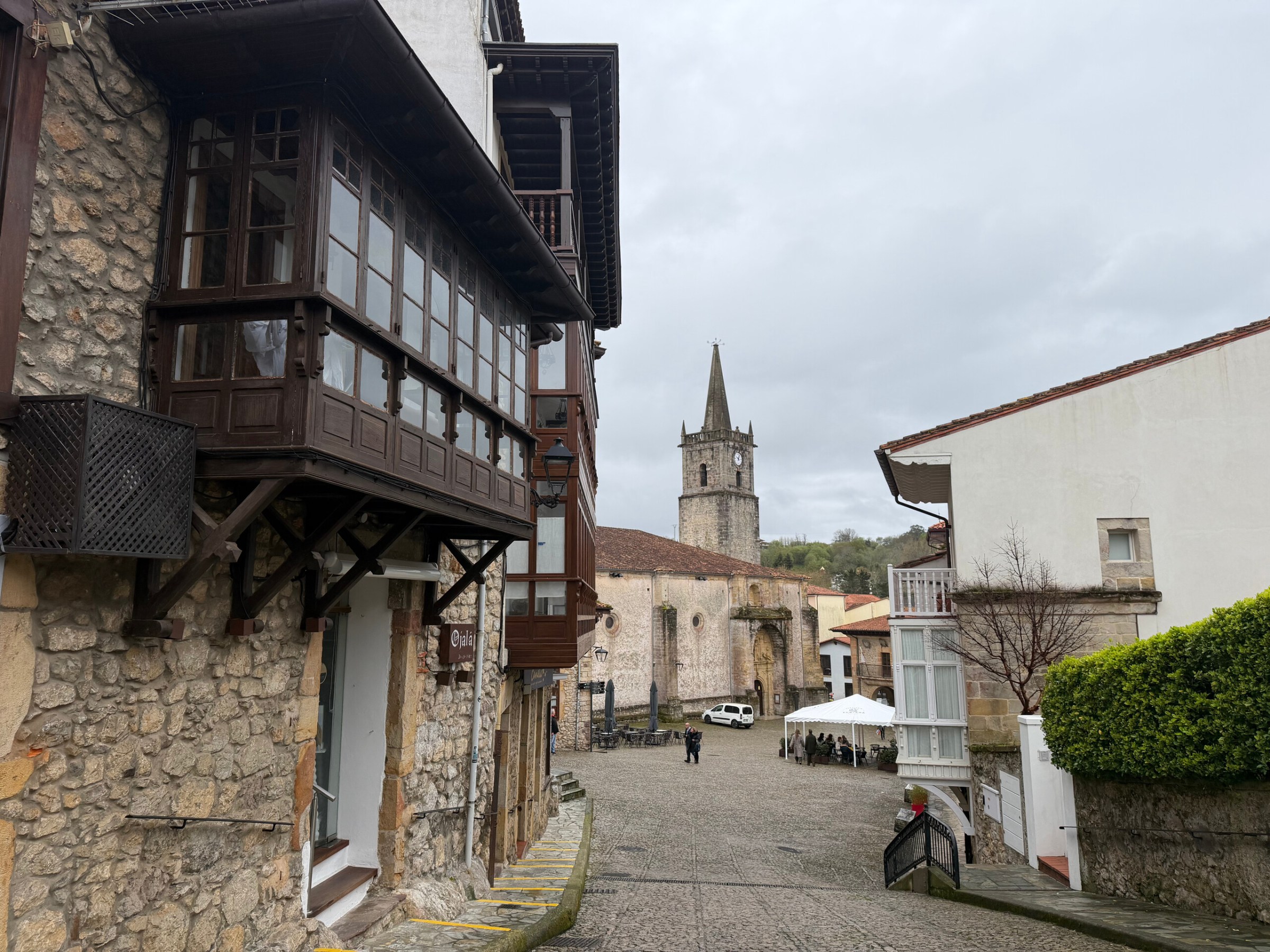 Historic street with stone buildings and distant church tower on a cloudy day.