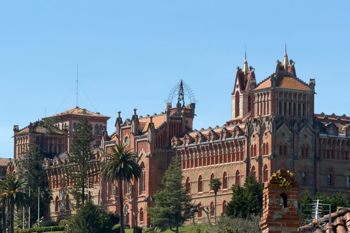 Historic red-brick building on a hill, blue sky background.