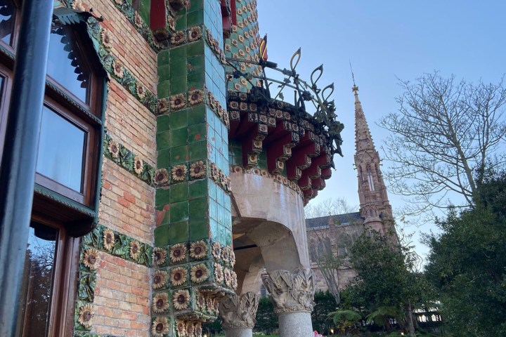 Ornate building with colorful tiles, balcony, spires, and a garden walkway.