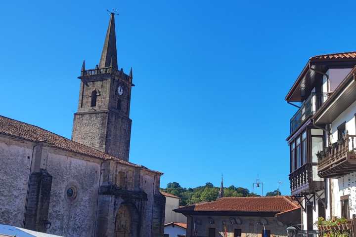 Outdoor market with umbrellas, people, and a church tower against a clear blue sky.