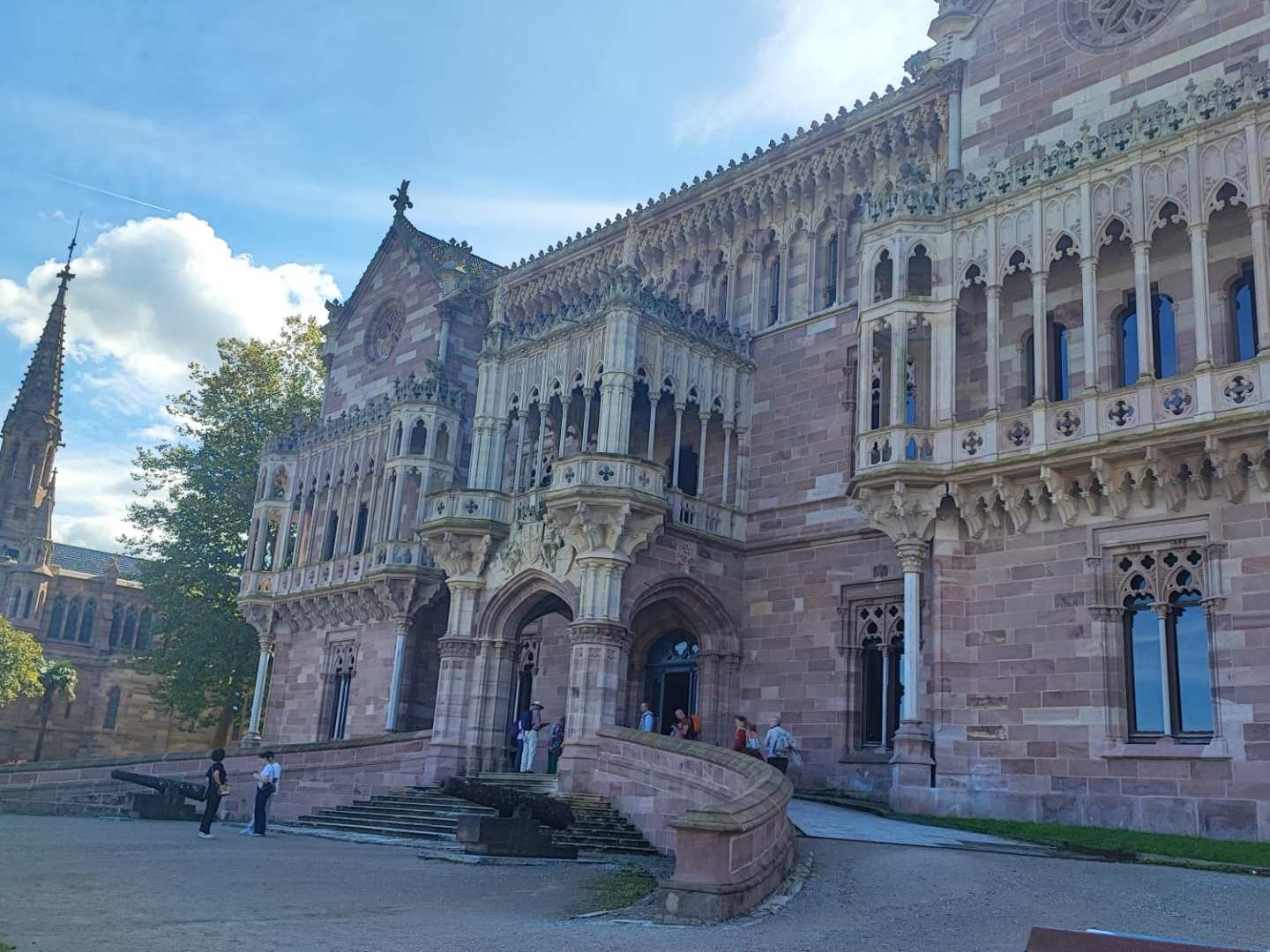 Gothic-style building with ornate facade and spire, people walking outside.