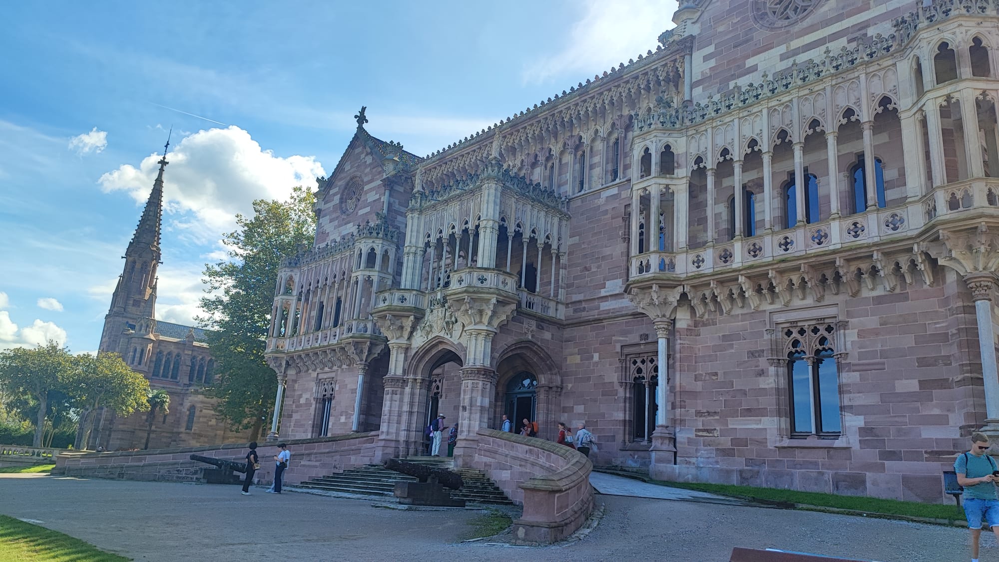 Gothic-style building with ornate facade and spire, people walking outside.