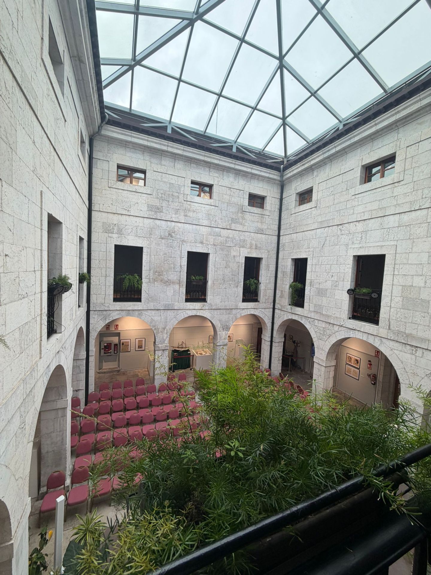 Courtyard with stone walls, red chairs, plants, and large glass ceiling.