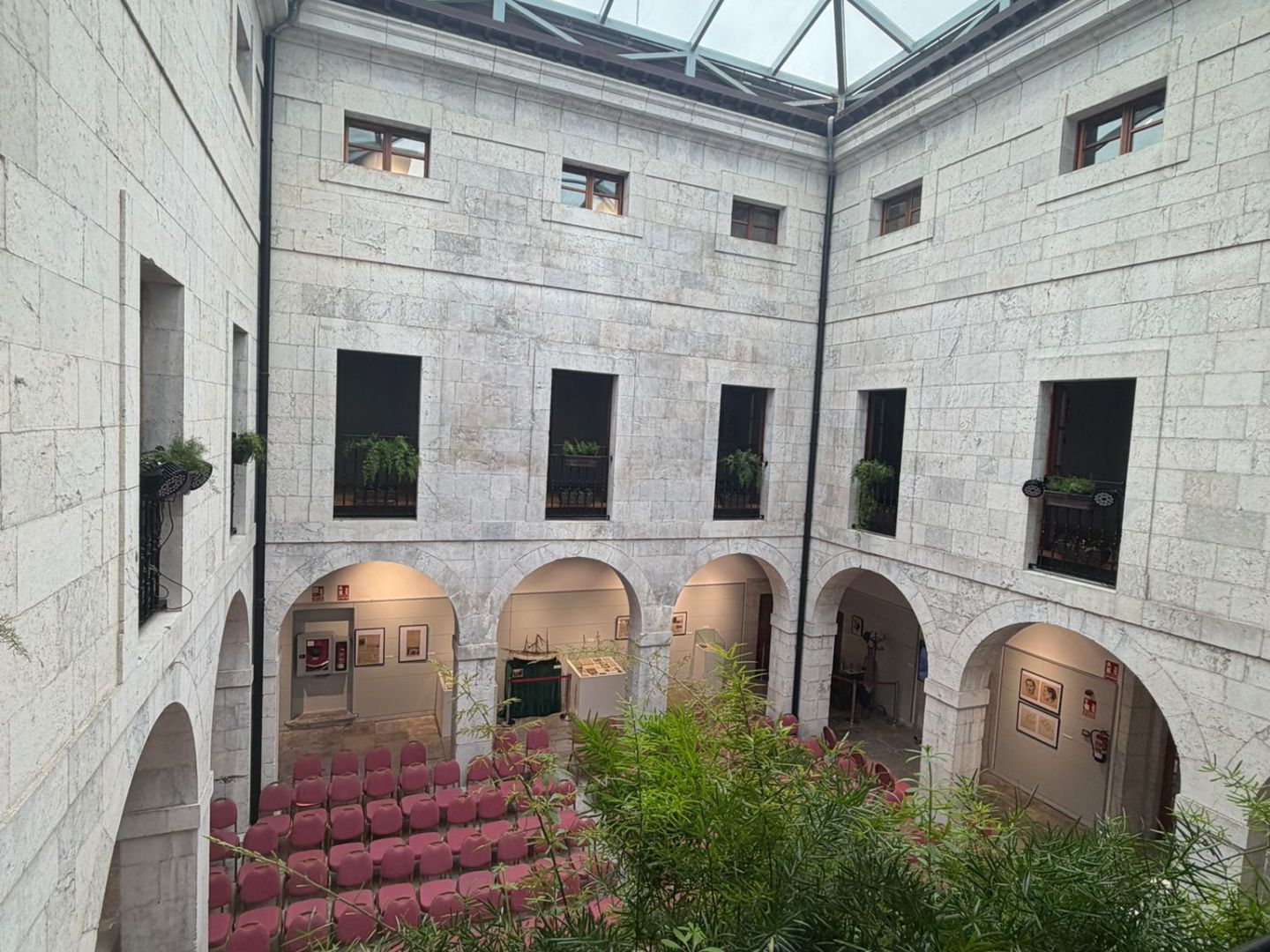 Courtyard with stone walls, red chairs, plants, and large glass ceiling.
