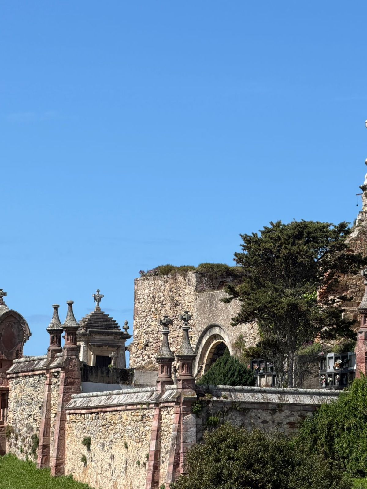 Historic stone wall and statue under blue sky, surrounded by greenery.