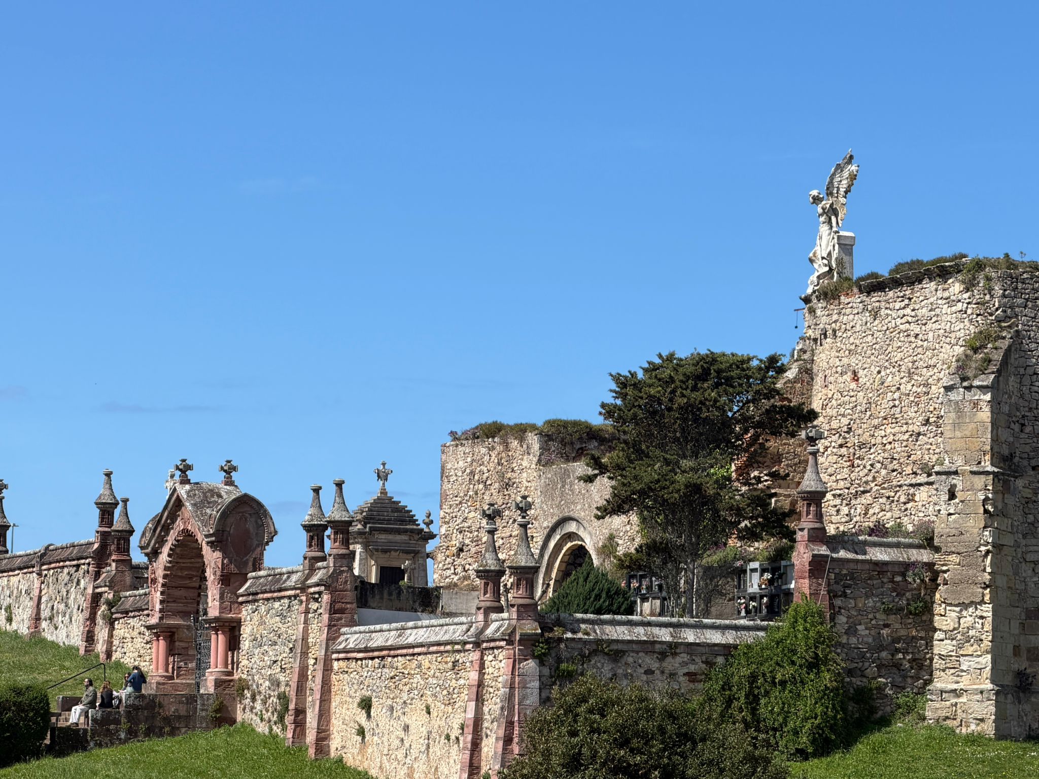 Historic stone wall and statue under blue sky, surrounded by greenery.