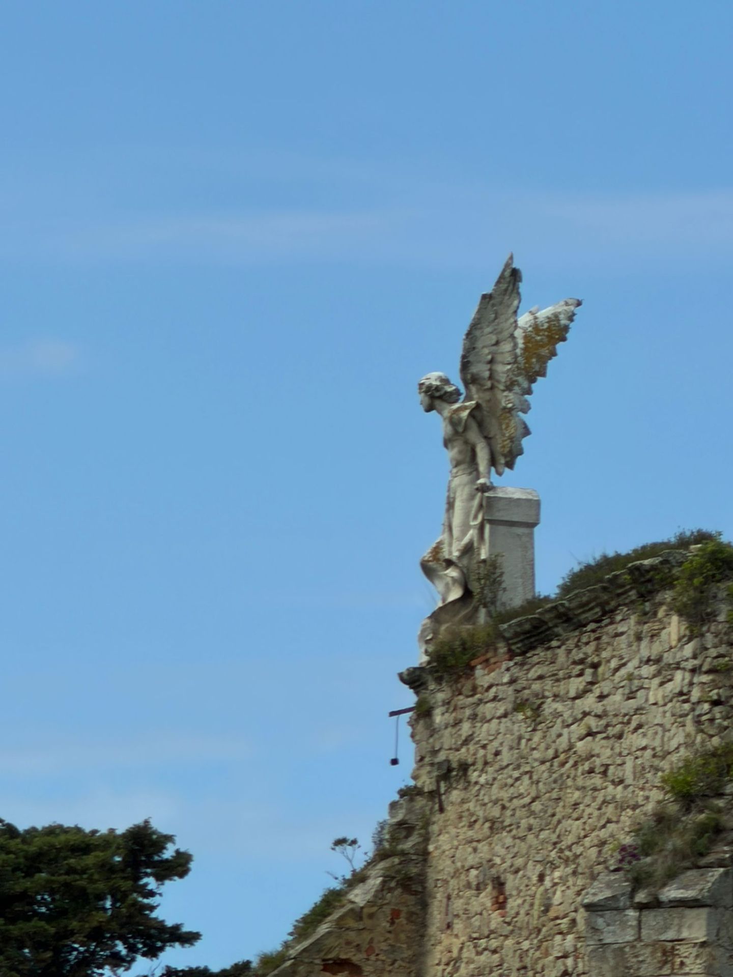 Stone angel statue with wings on a wall against blue sky