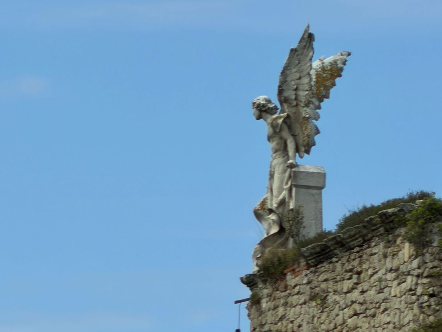 Stone angel statue with wings on a wall against blue sky