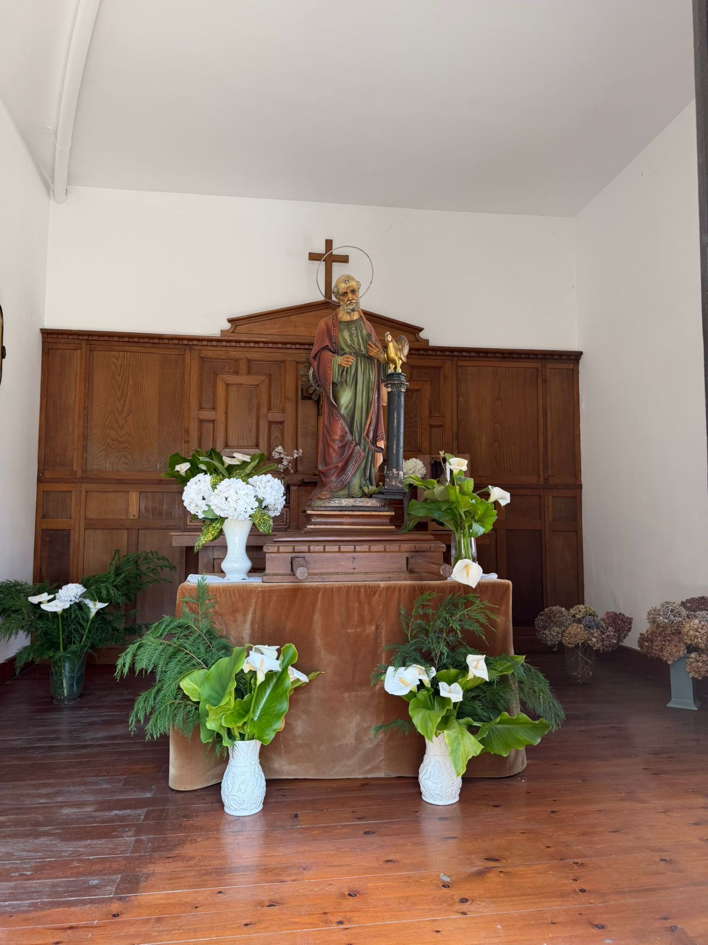 Statue in a chapel with flowers and wooden paneling.