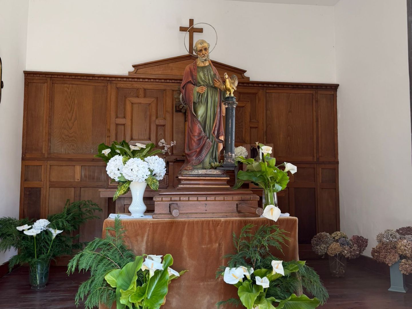 Statue in a chapel with flowers and wooden paneling.