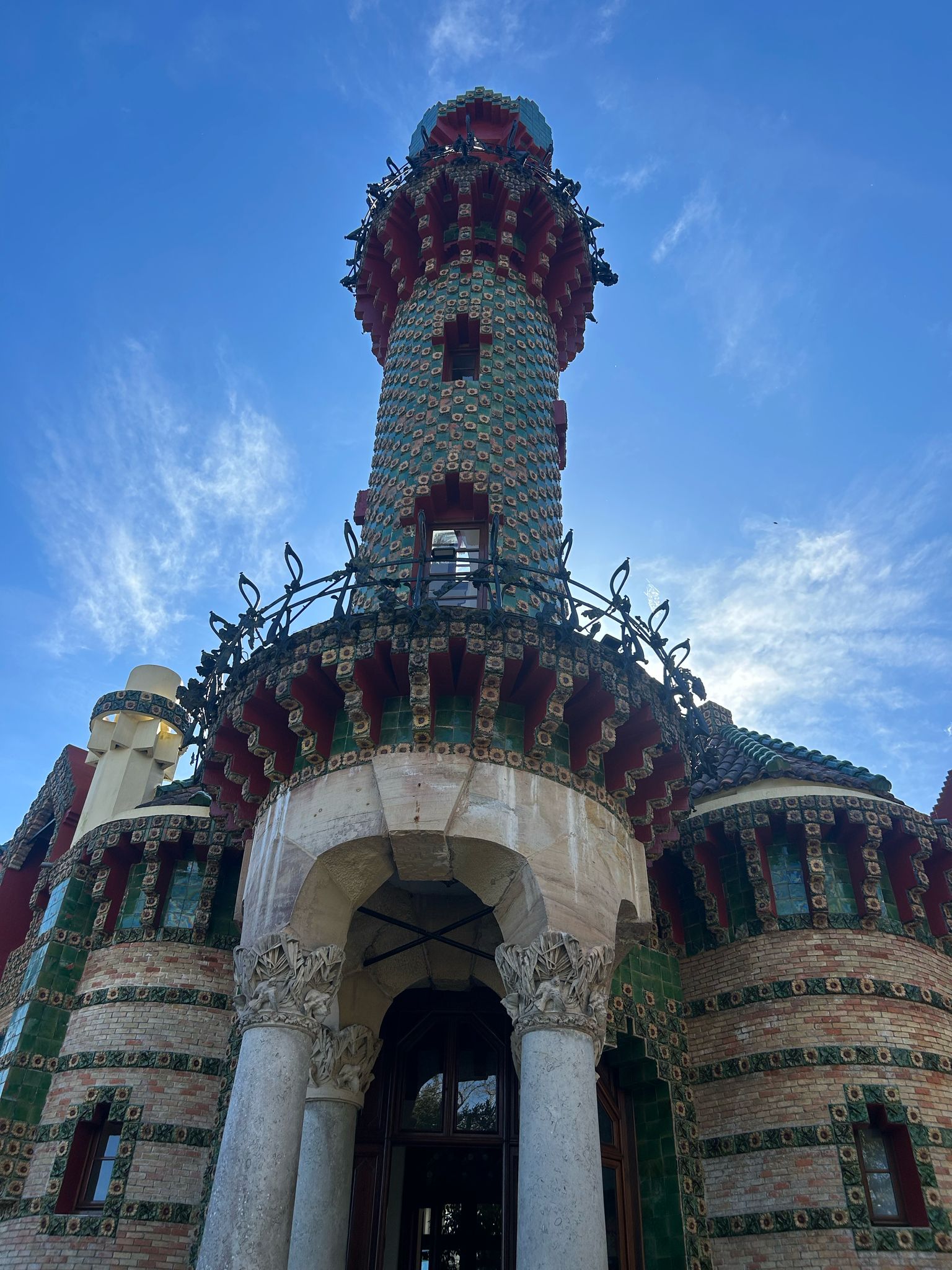 Colorful eclectic tower with mosaic patterns against a blue sky.