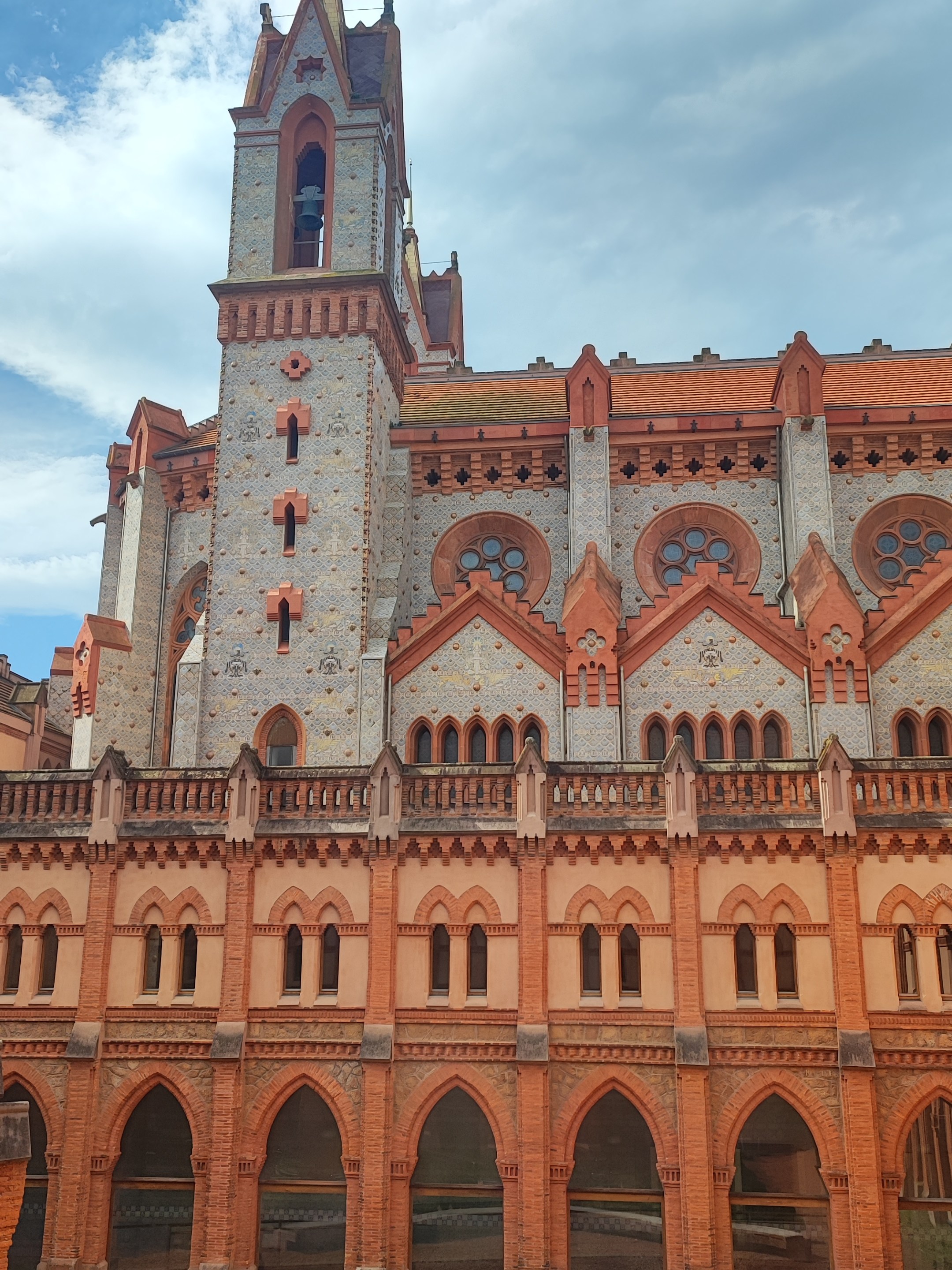 Gothic-style building with red brick arches and a tower under a blue sky.
