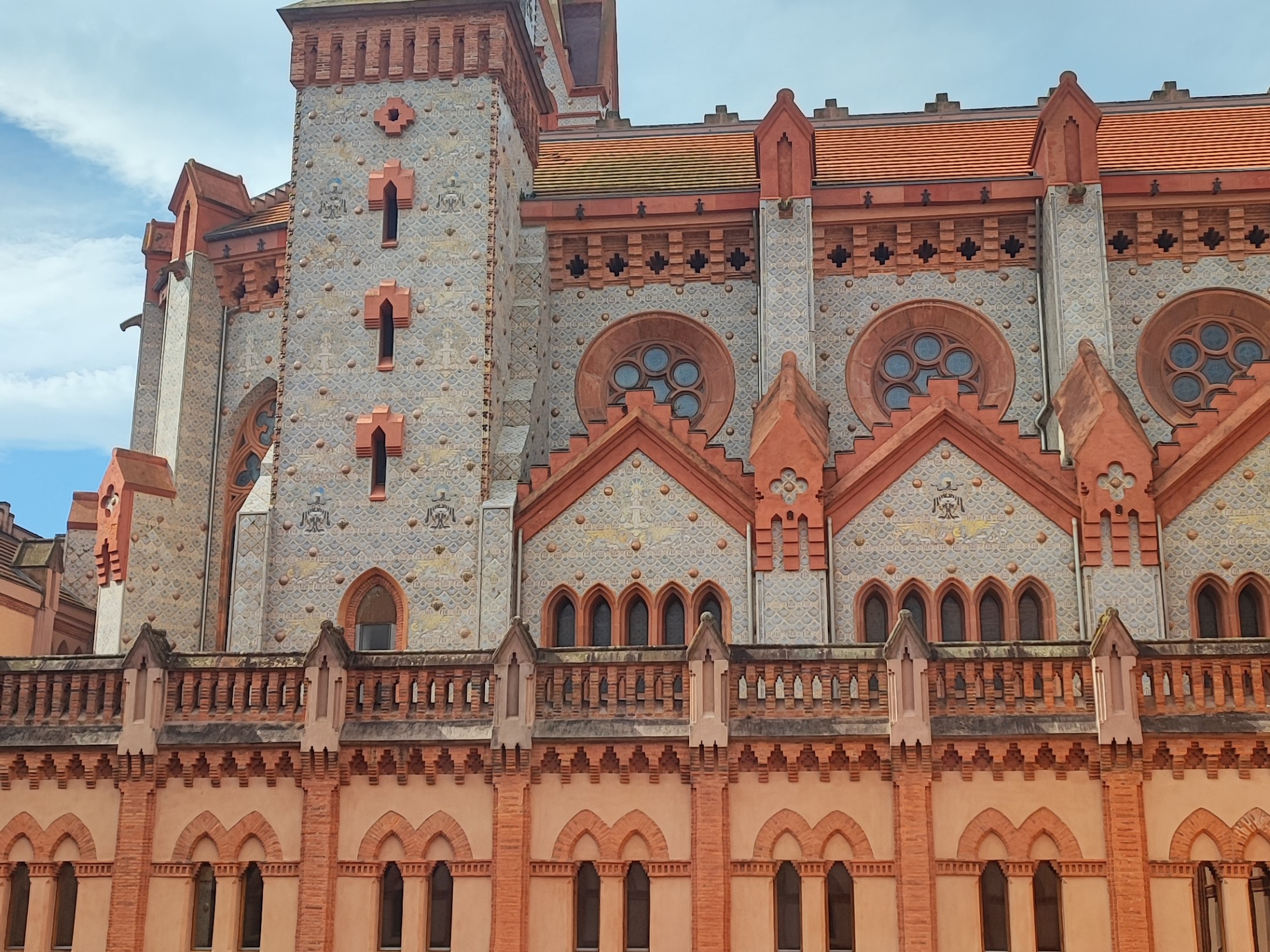 Gothic-style building with red brick arches and a tower under a blue sky.
