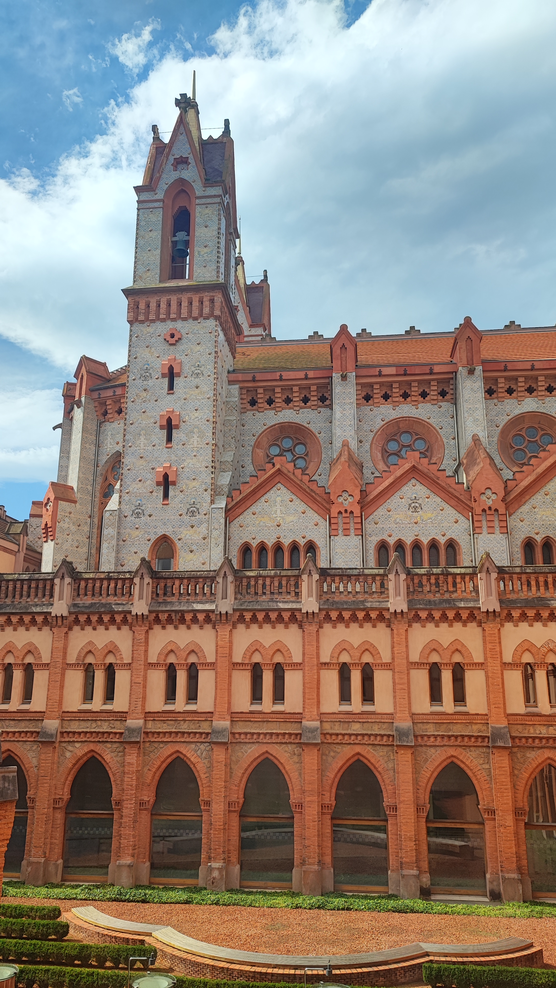 Gothic-style building with red brick arches and a tower under a blue sky.