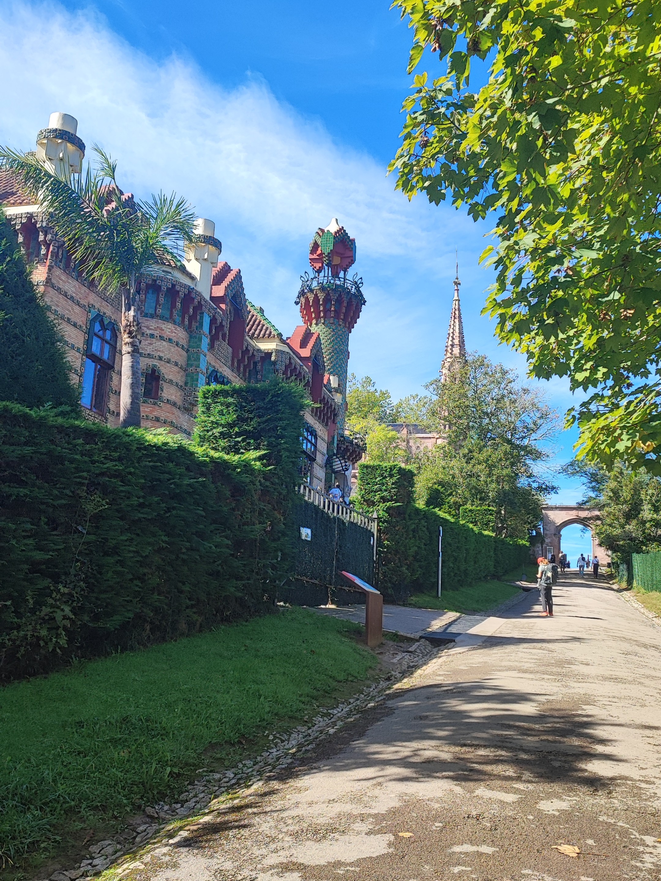 Path lined with greenery, ornate building, blue sky, and cyclist.