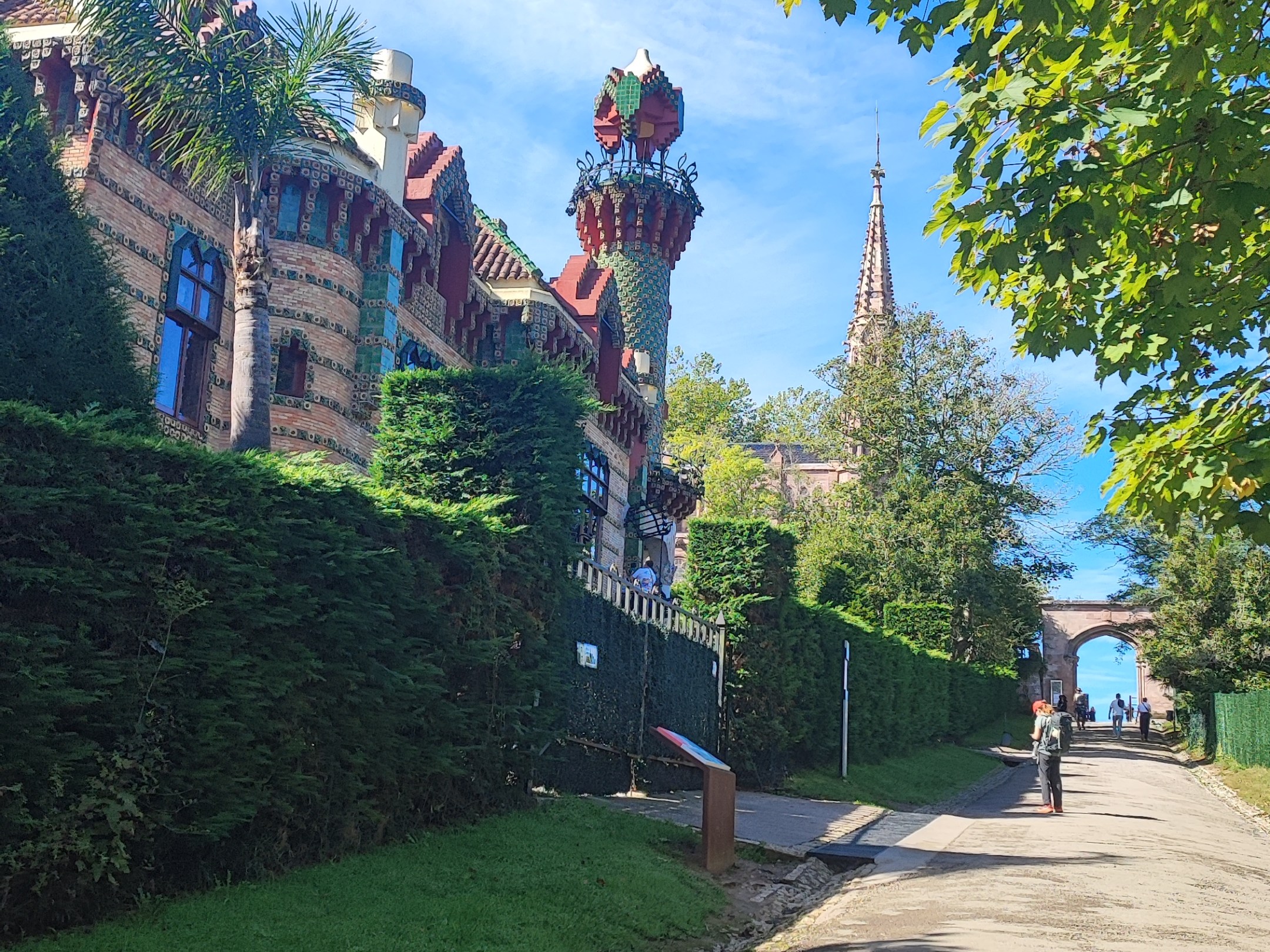 Path lined with greenery, ornate building, blue sky, and cyclist.