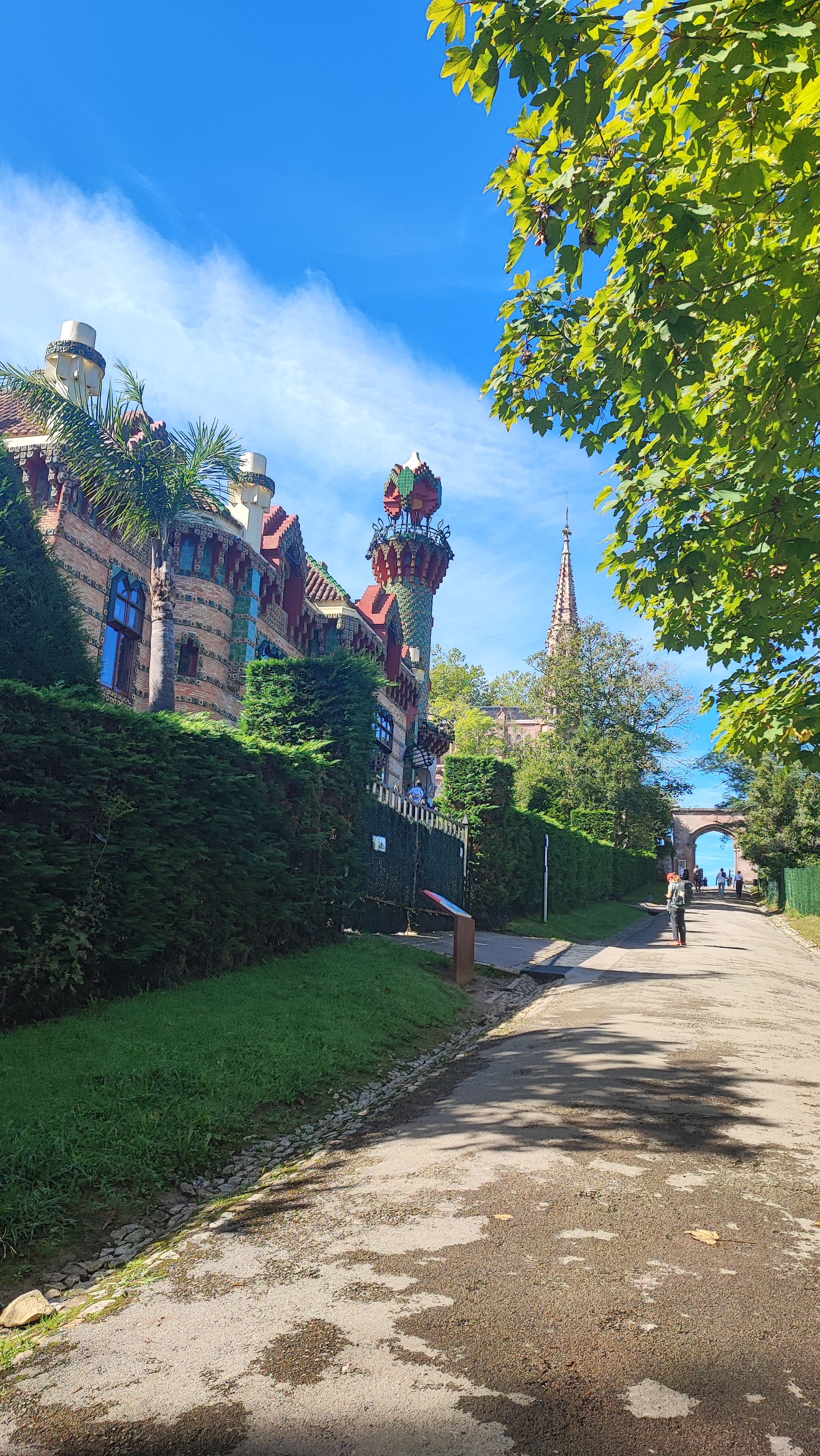 Path lined with greenery, ornate building, blue sky, and cyclist.