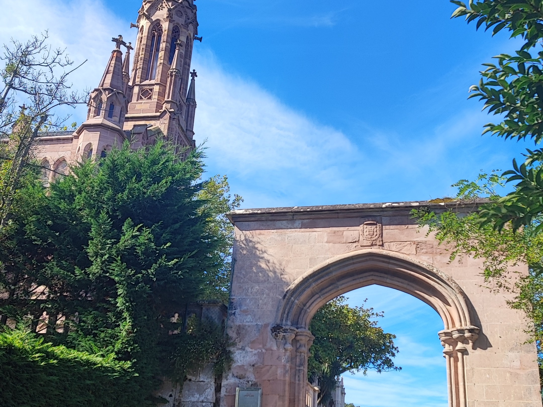 Stone archway and church spire under blue sky, person walking.