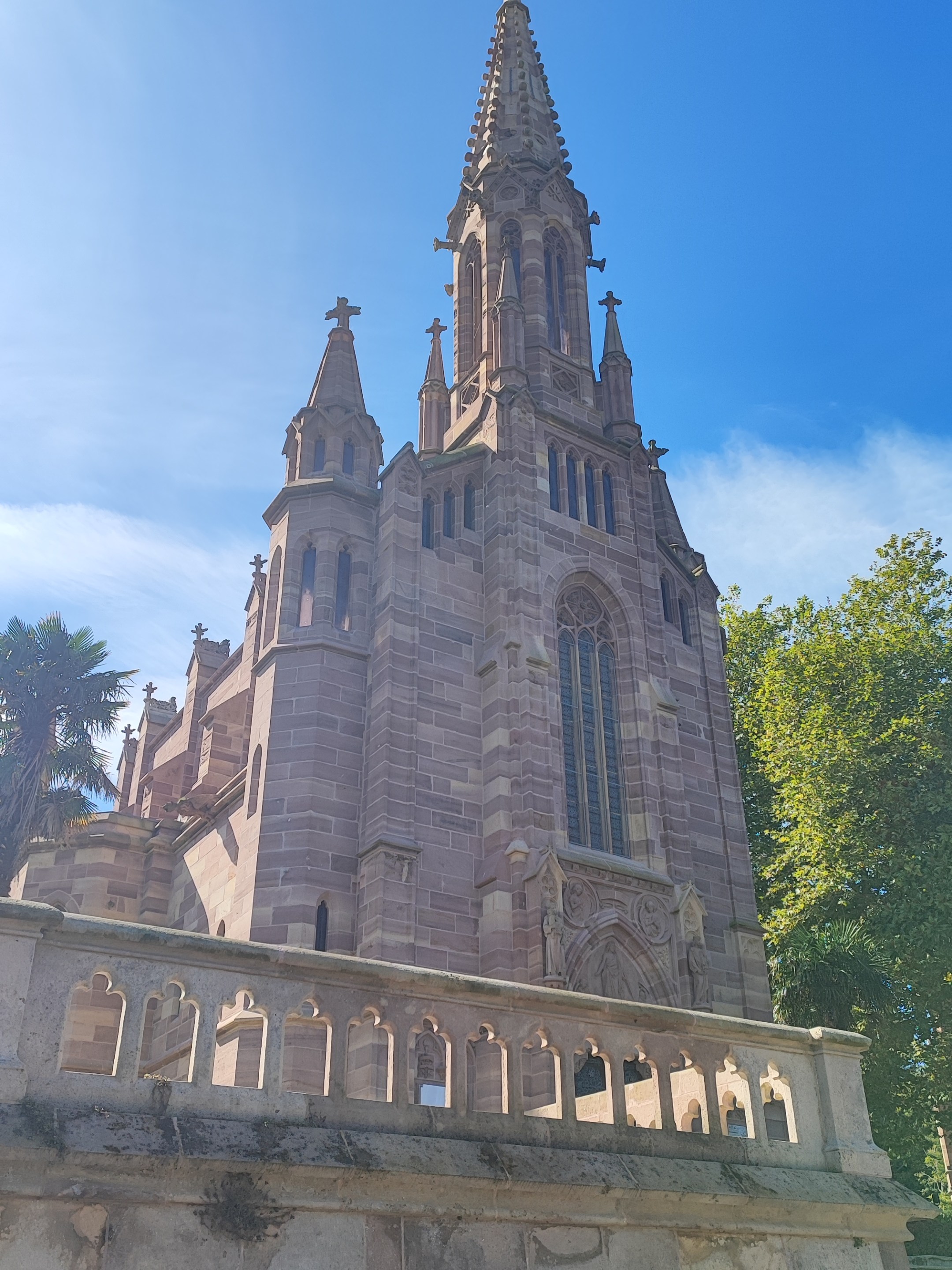 Gothic-style stone church with tall spire, sunny sky.