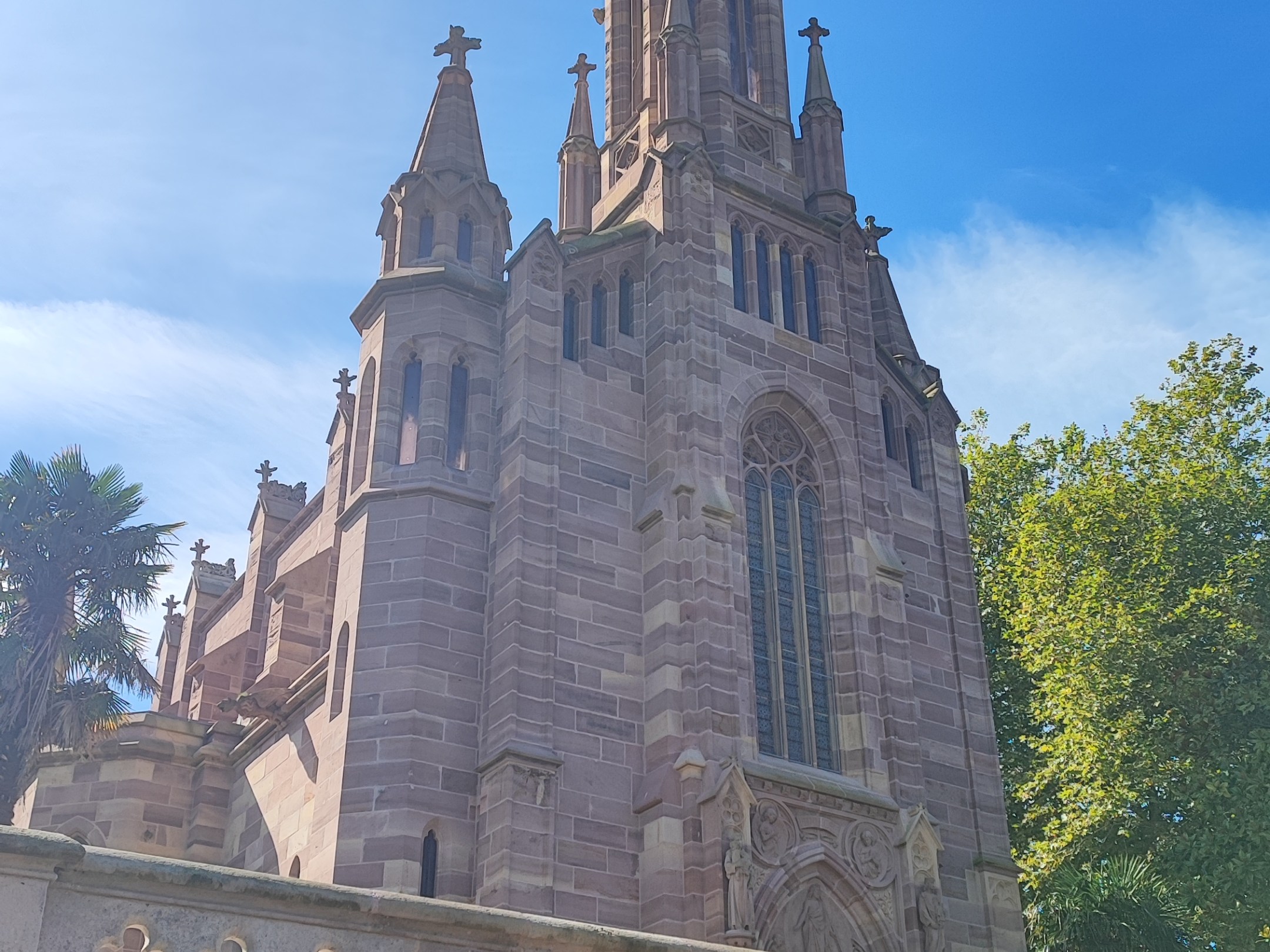 Gothic-style stone church with tall spire, sunny sky.