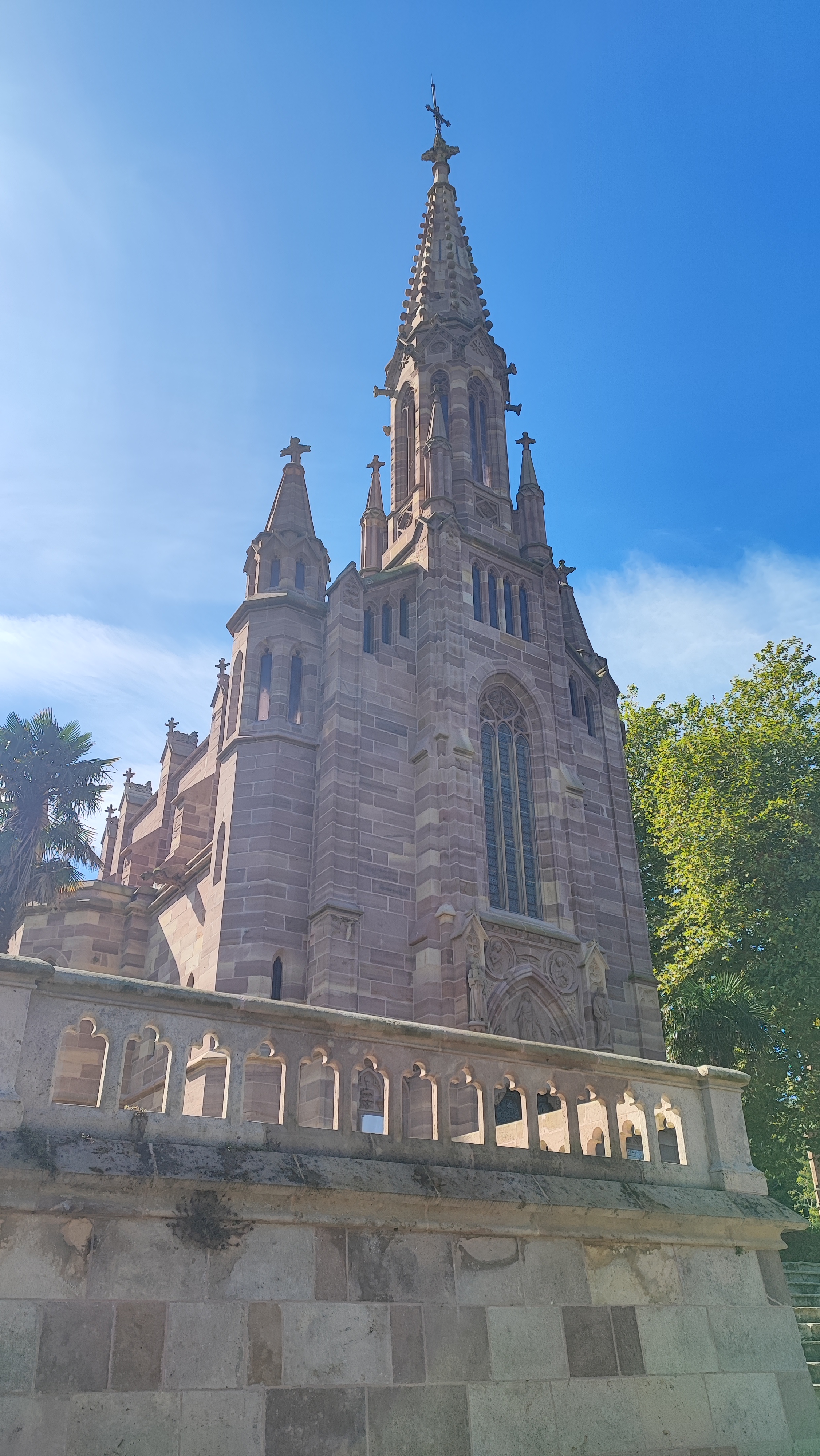 Gothic-style stone church with tall spire, sunny sky.
