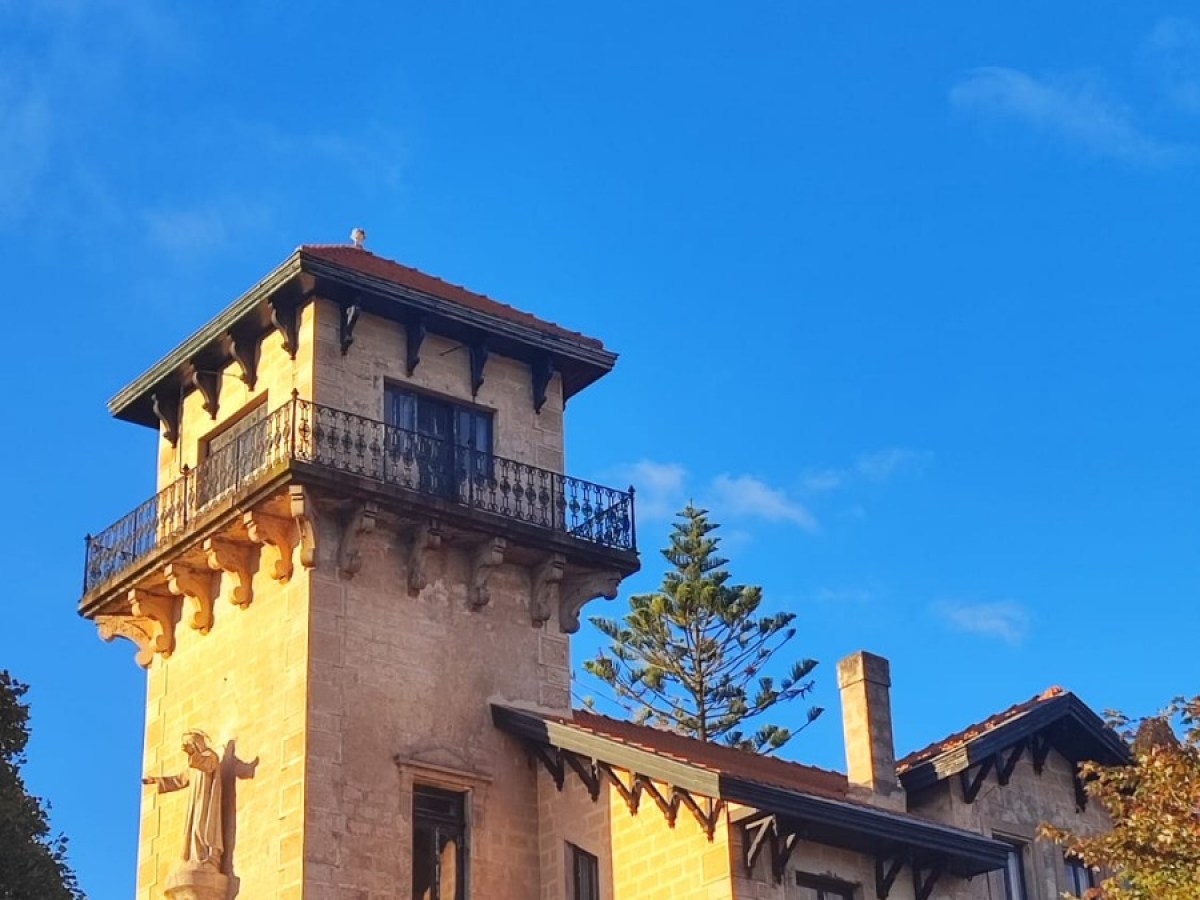 Historic building with a tall tower and ornate balcony under a clear blue sky.