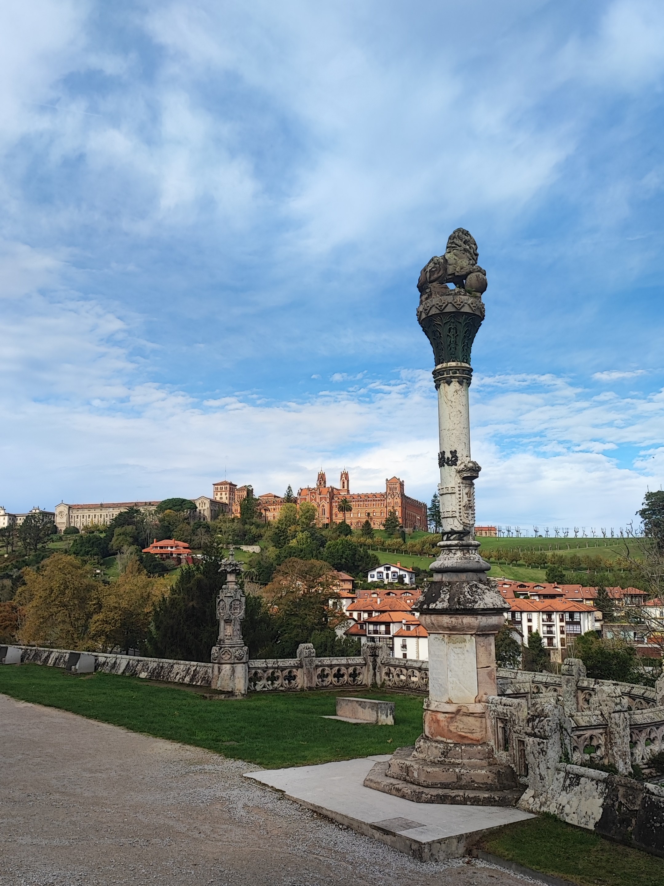Stone column and statues with castle in the distance under a cloudy blue sky.