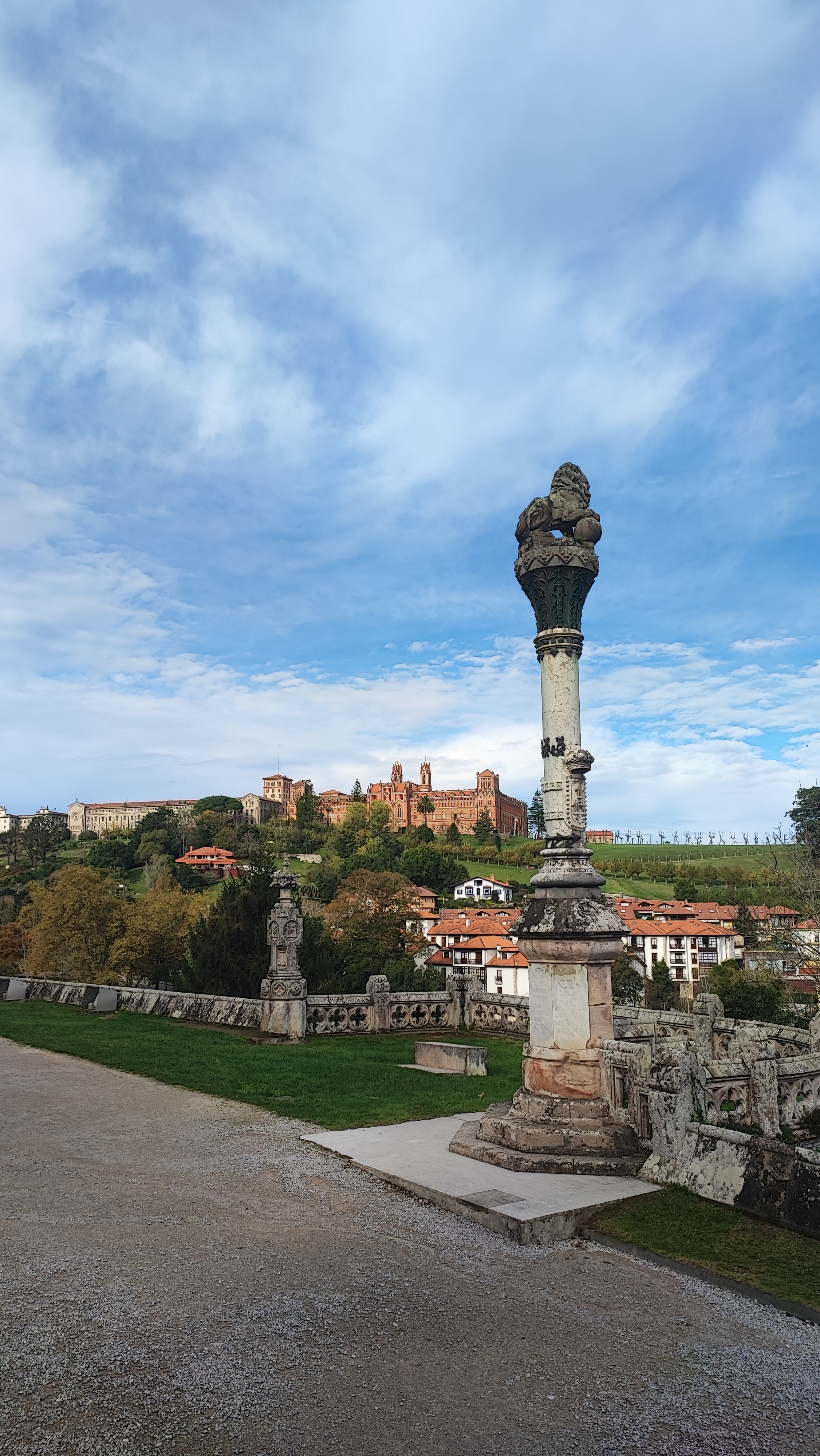Stone column and statues with castle in the distance under a cloudy blue sky.