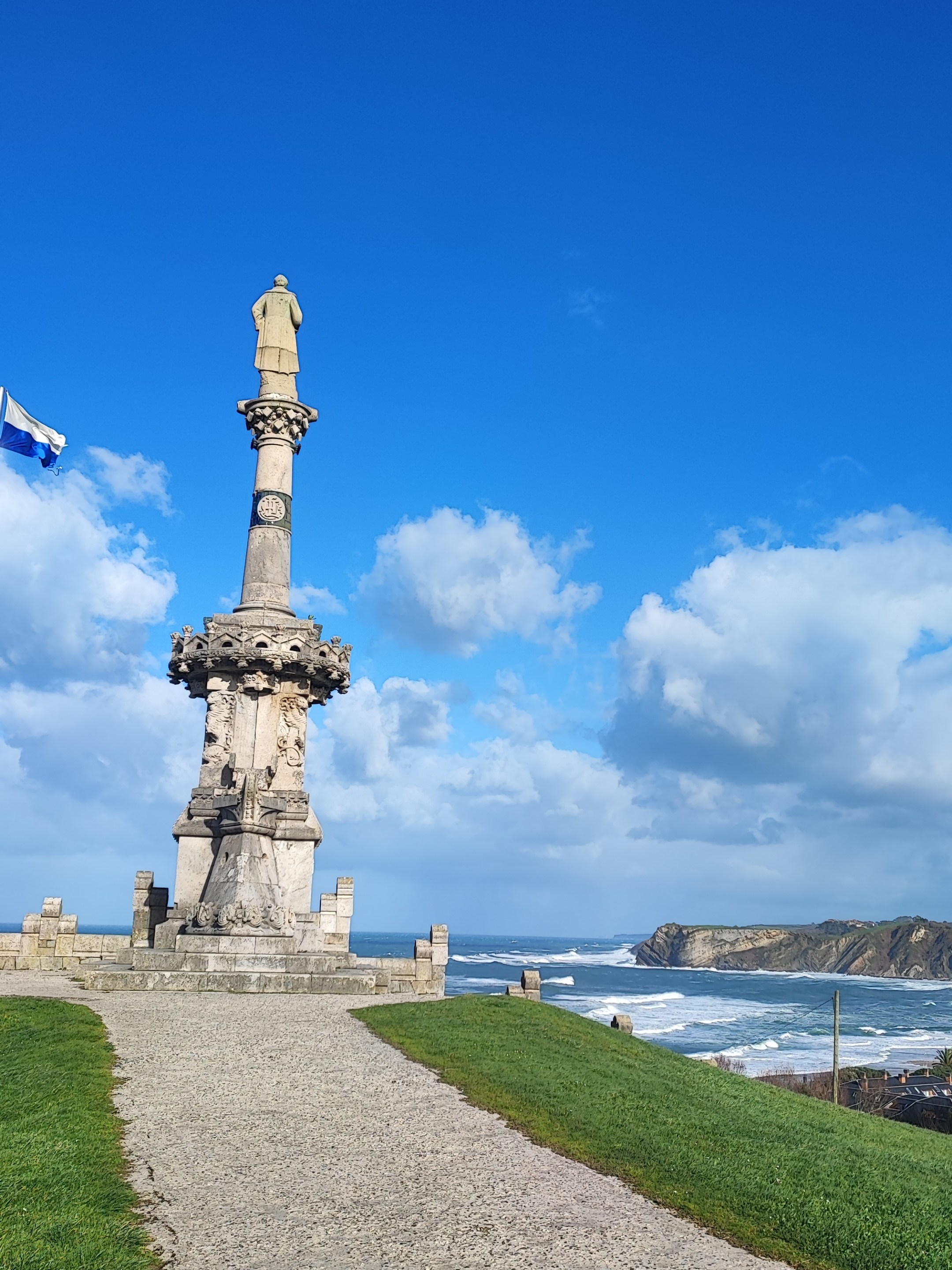 Tall stone monument on coastal path with blue sky and ocean view