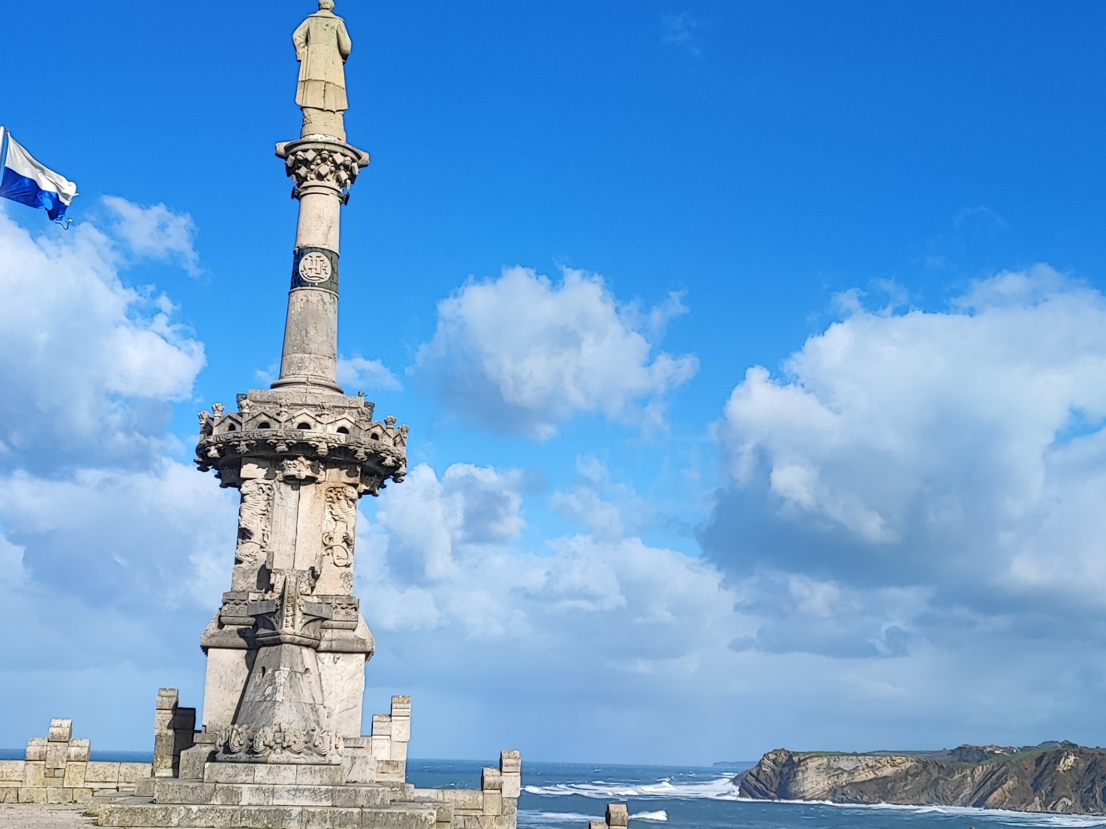 Tall stone monument on coastal path with blue sky and ocean view