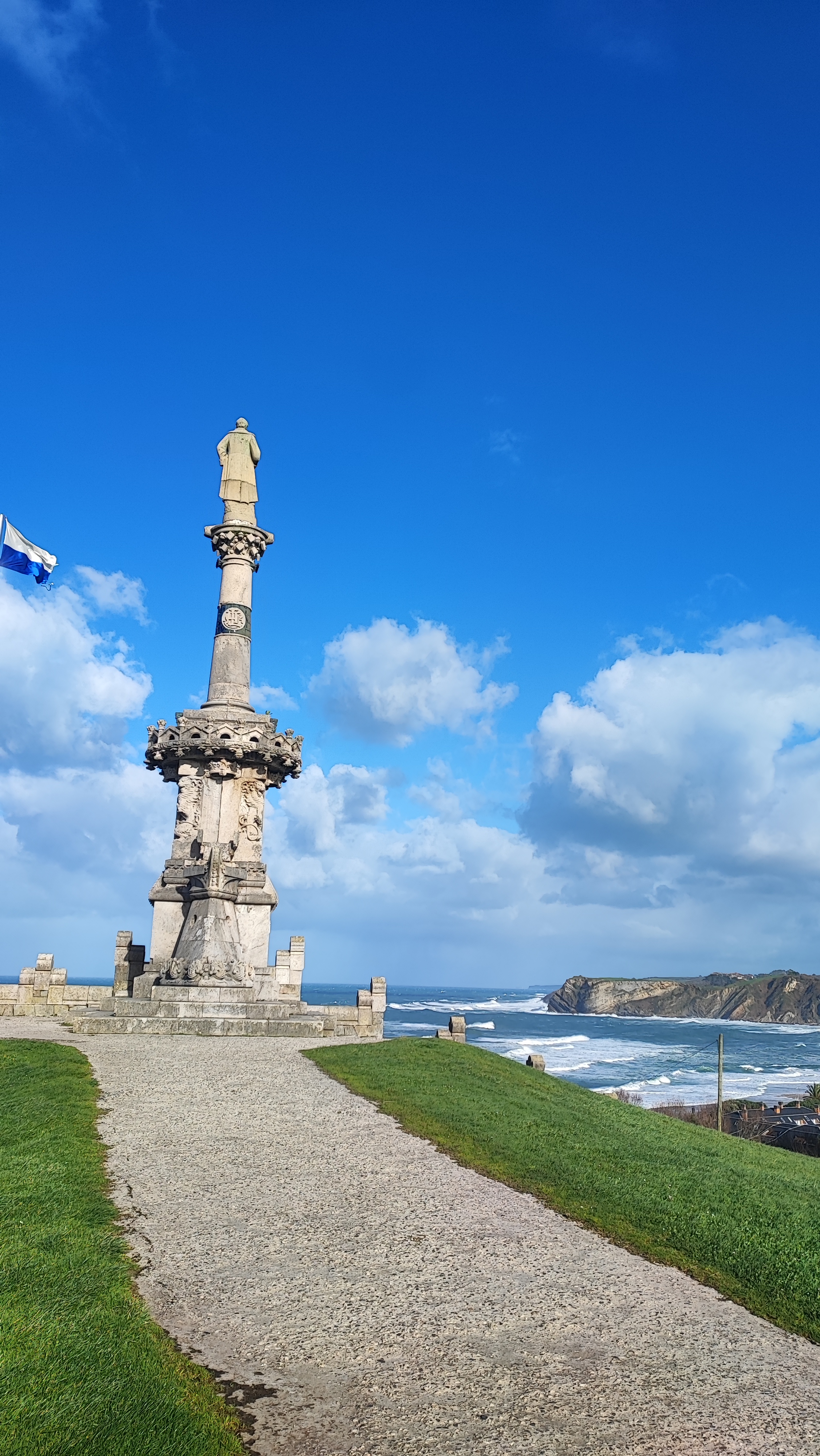 Tall stone monument on coastal path with blue sky and ocean view