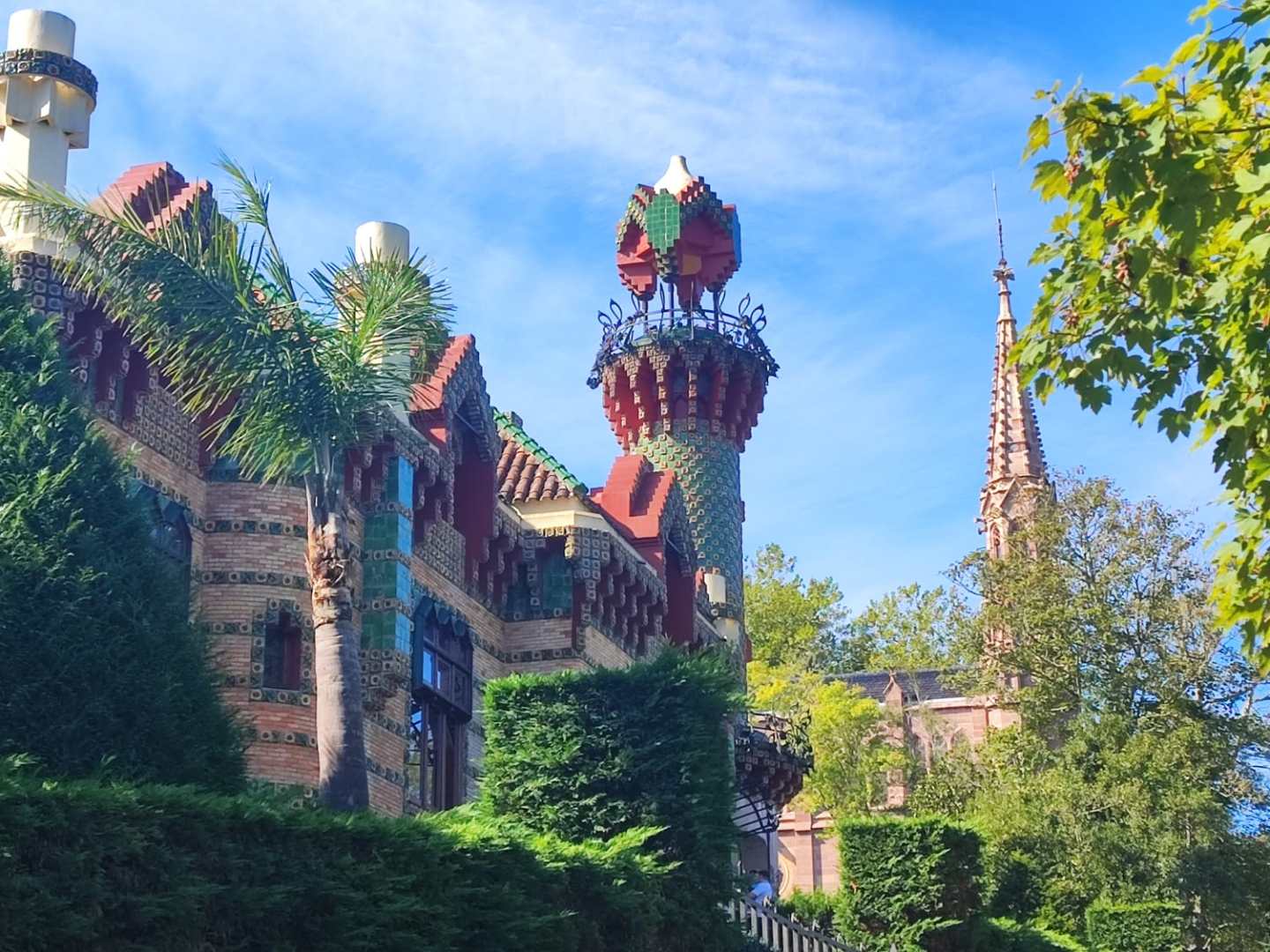 Colorful and ornate building with tower, surrounded by trees under a blue sky.