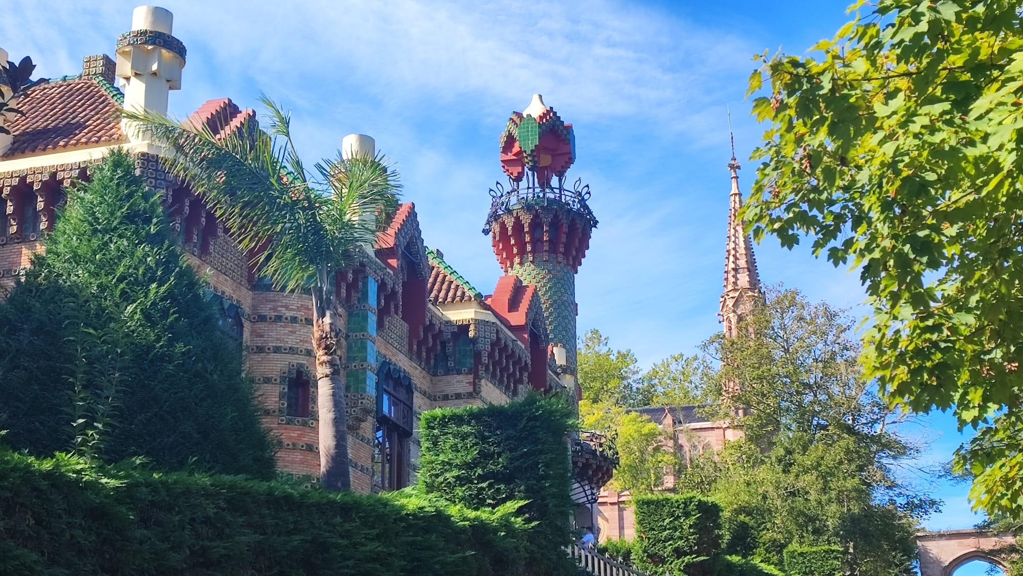 Colorful and ornate building with tower, surrounded by trees under a blue sky.