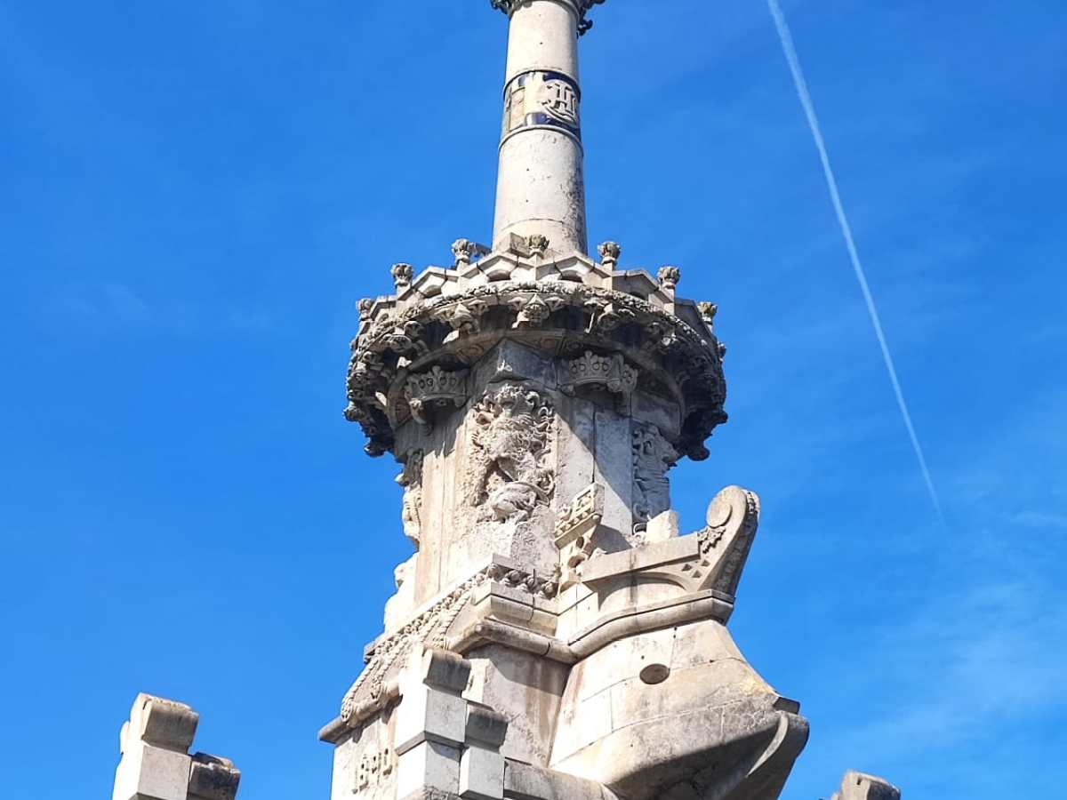 Tall stone monument with statue atop, clear blue sky background.