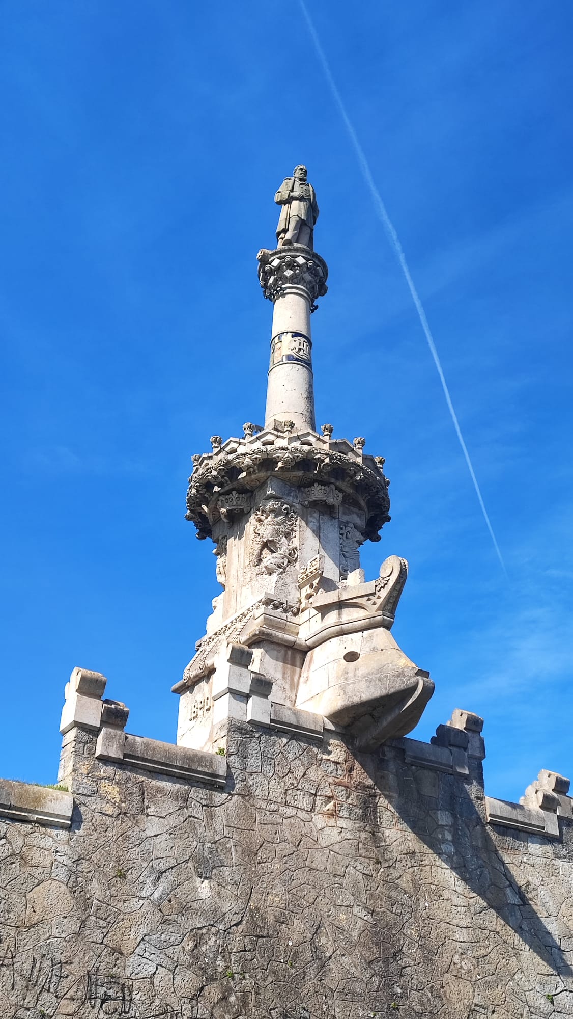 Tall stone monument with statue atop, clear blue sky background.