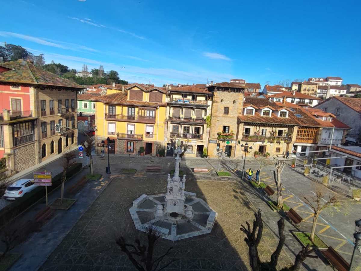 Scenic town square with colorful buildings around a central statue and fountain.