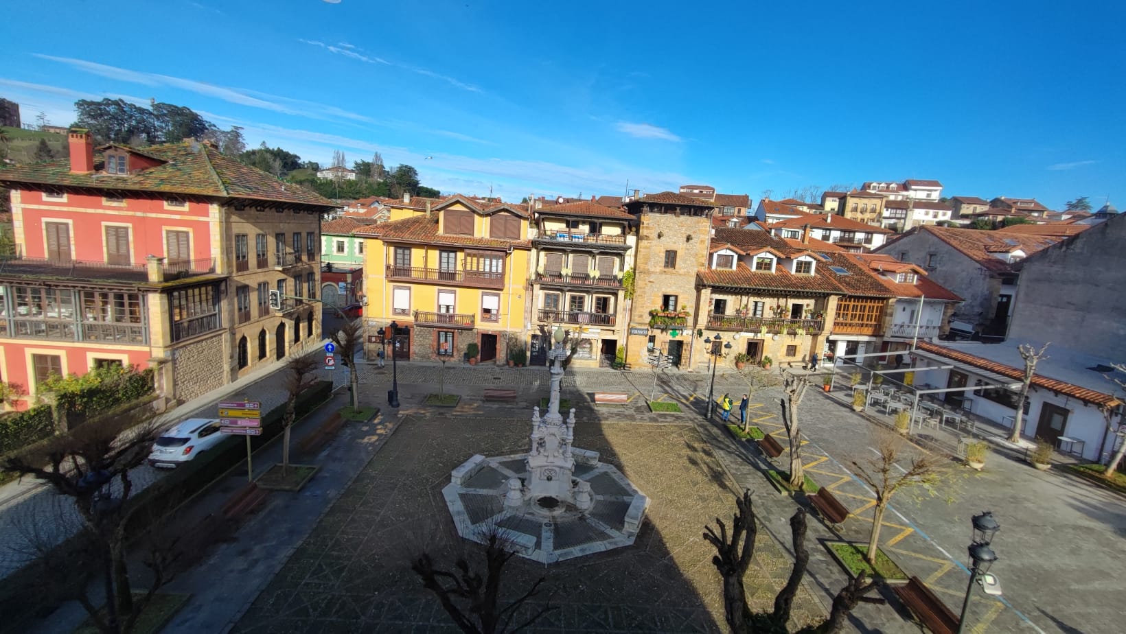 Scenic town square with colorful buildings around a central statue and fountain.