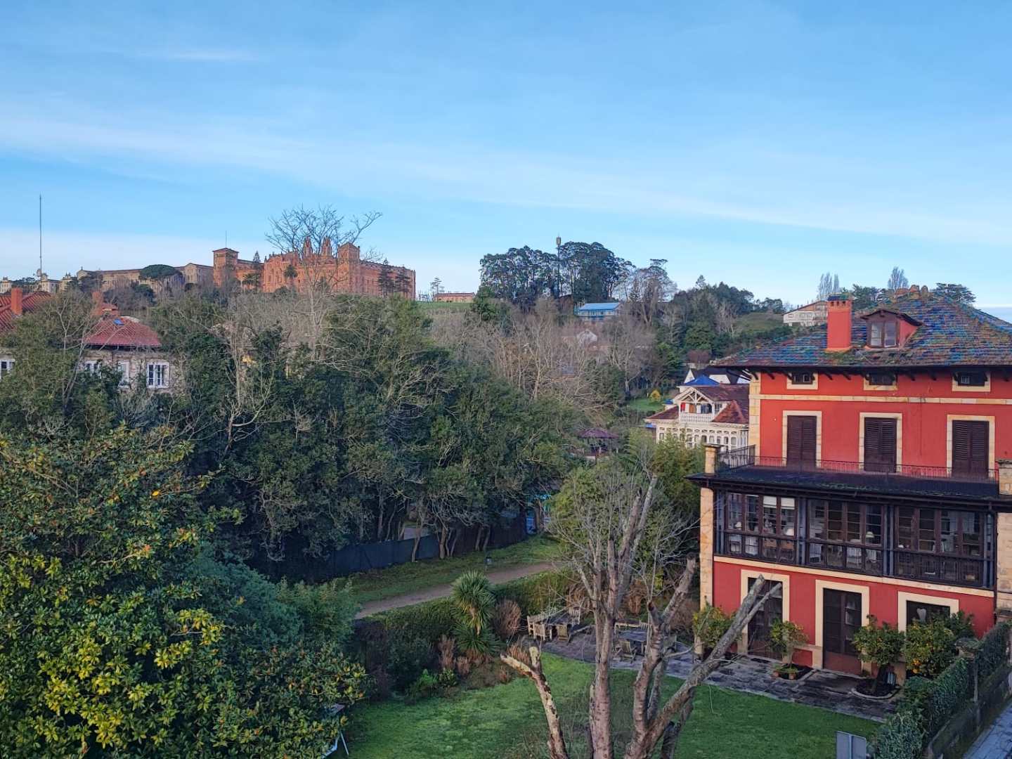 A scenic view of a red building, trees, and a distant castle under a blue sky.