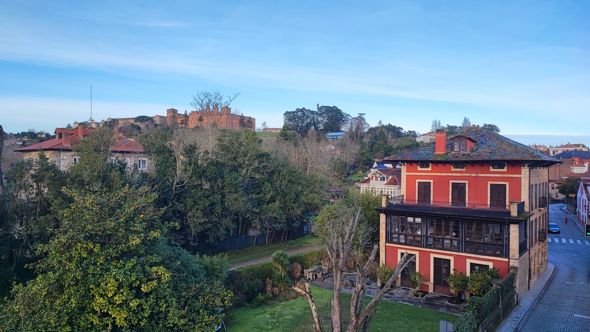 A scenic view of a red building, trees, and a distant castle under a blue sky.