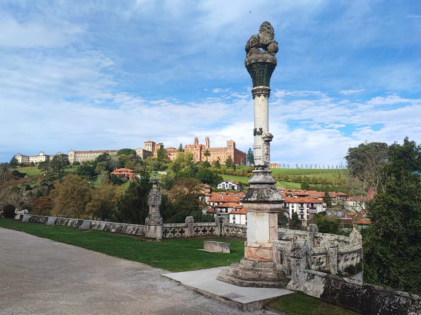Stone pillar with scenic view of a hilltop village in the background under a blue sky.