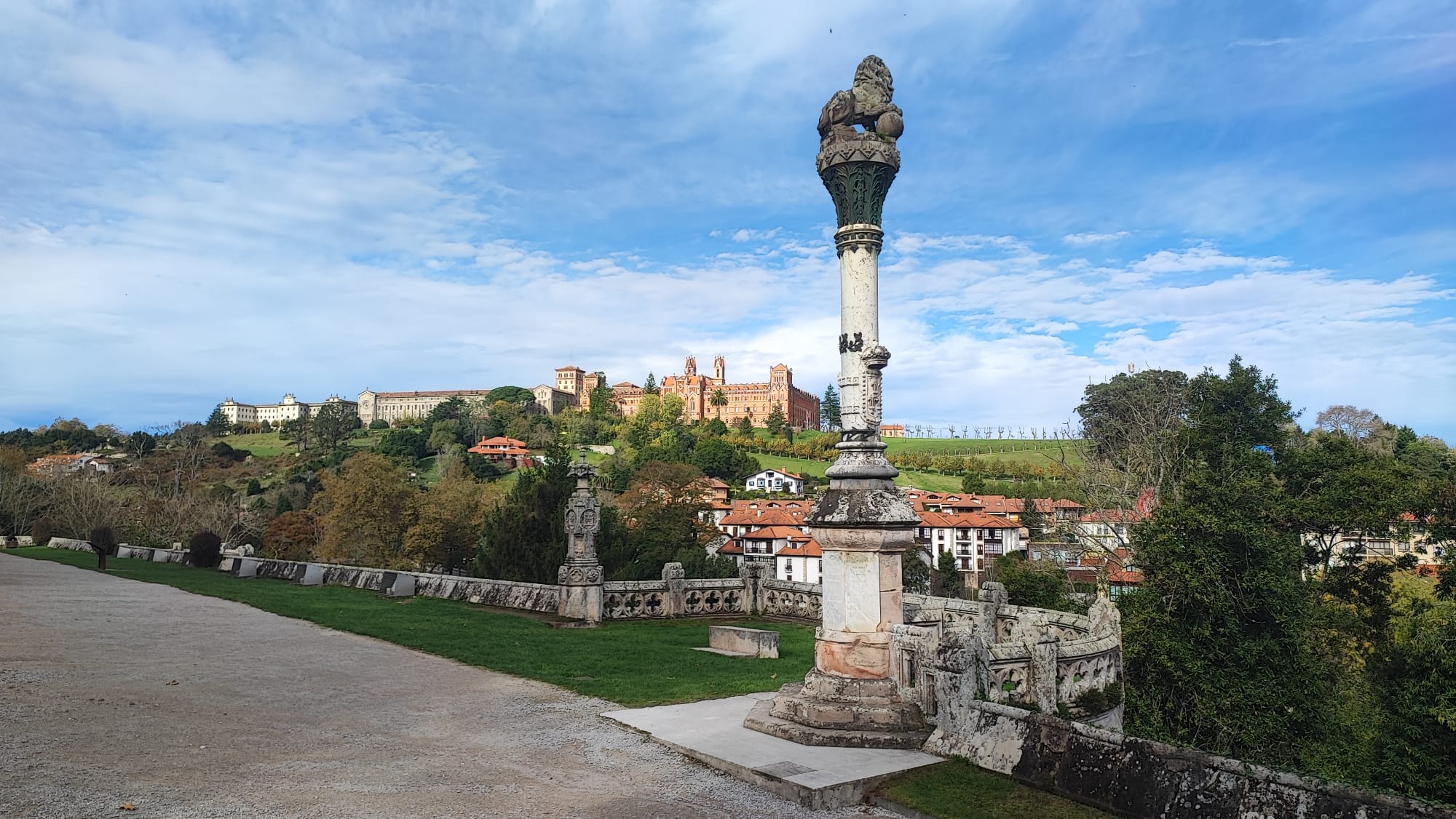 Stone pillar with scenic view of a hilltop village in the background under a blue sky.